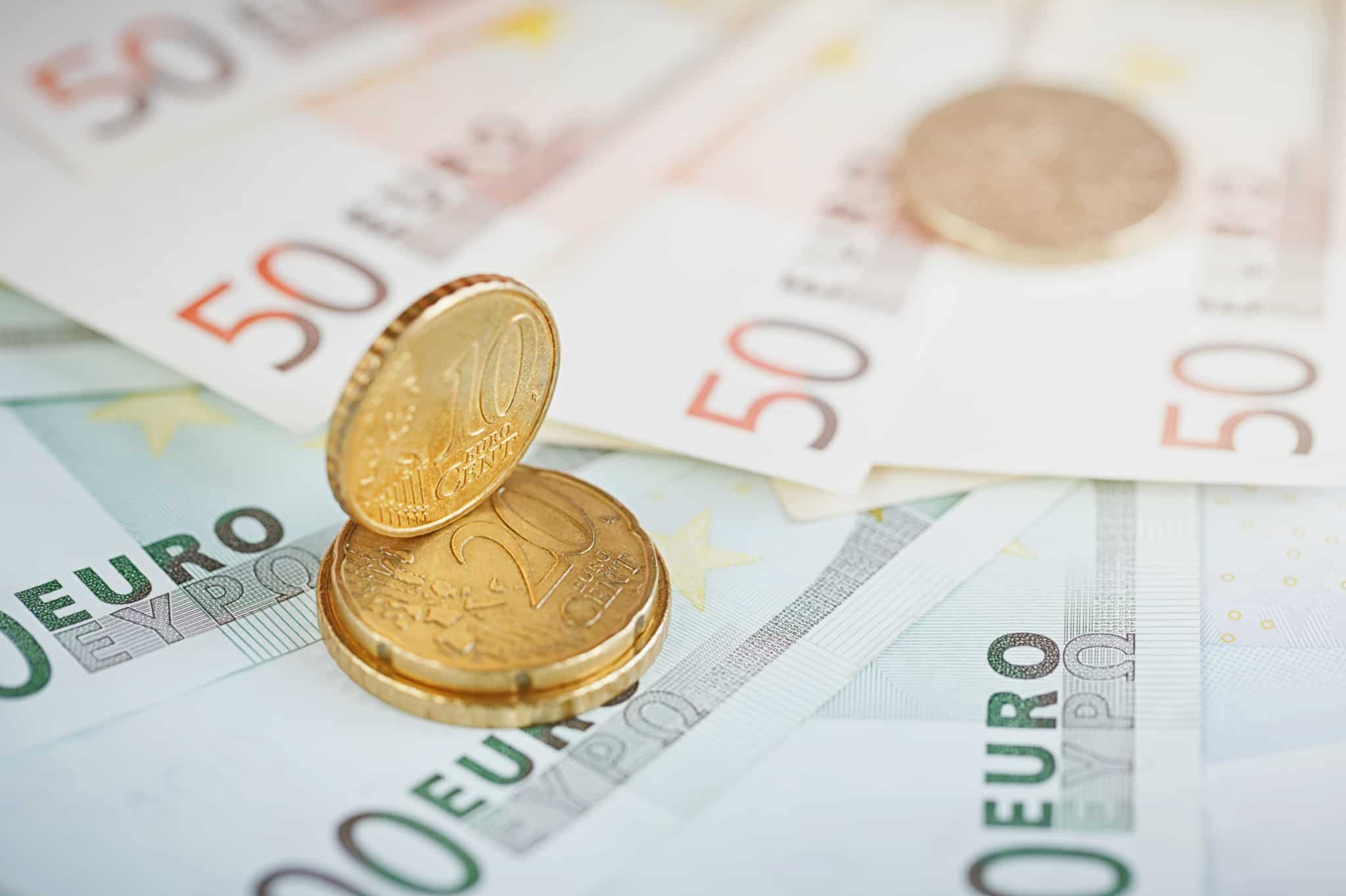 Poupança. notas de 20 e 50 euros espalhadas numa mesa. Em cima estão três moedas de 50 cêntimos