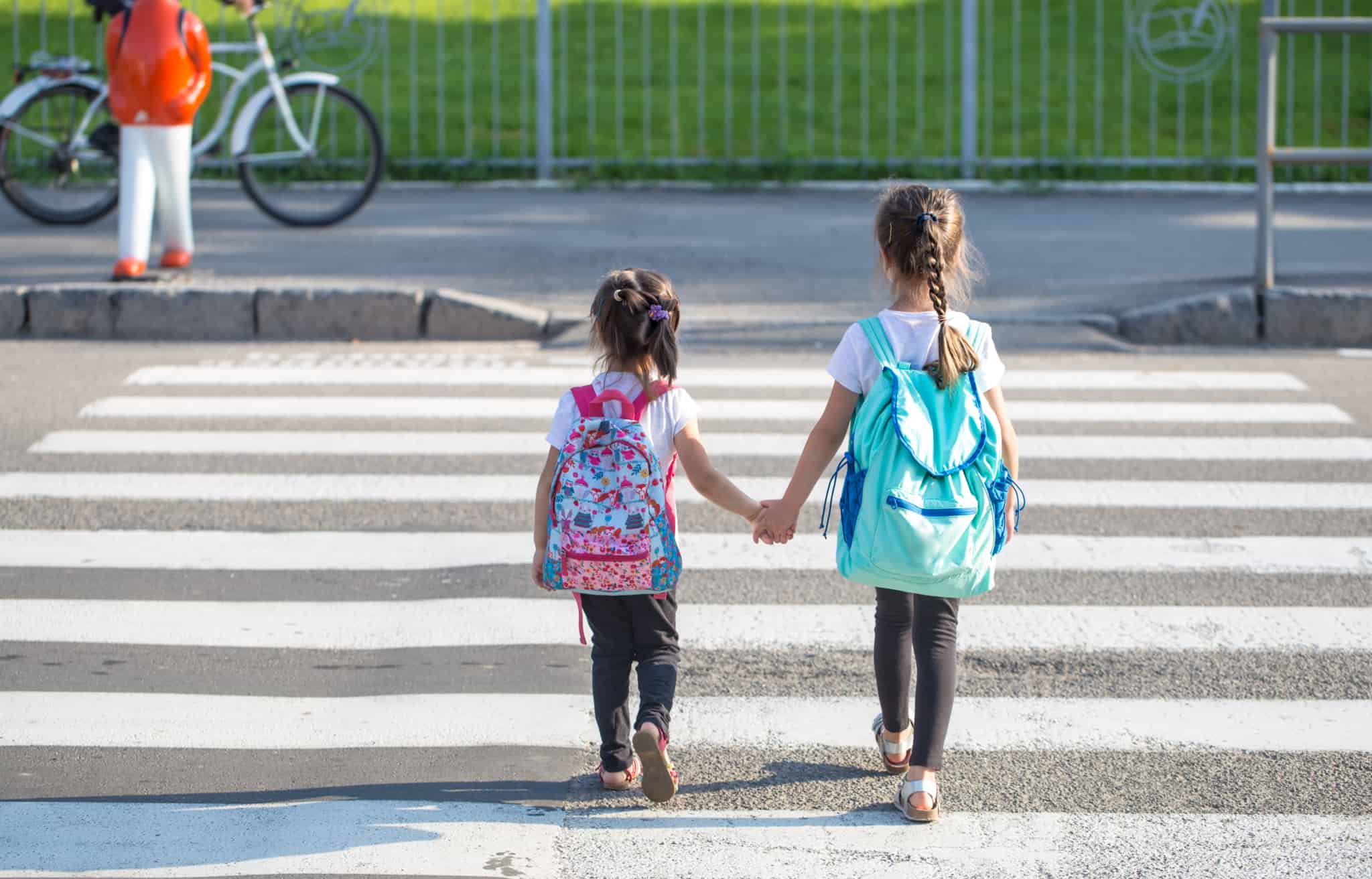 duas crianças a atravessar passadeira carregam mochila alertando para poupar no regresso às aulas