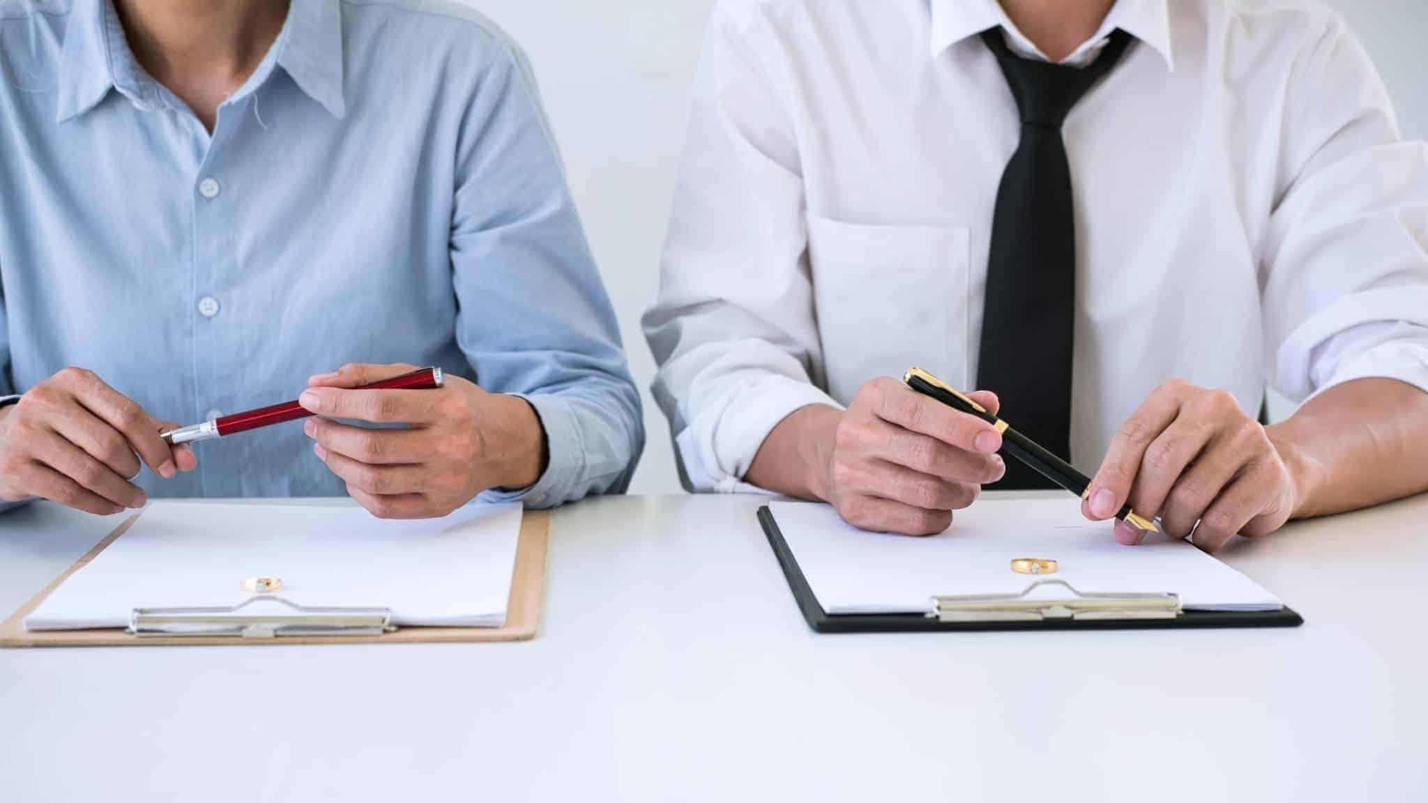 dois homens a segurar canetas para assinar contratos