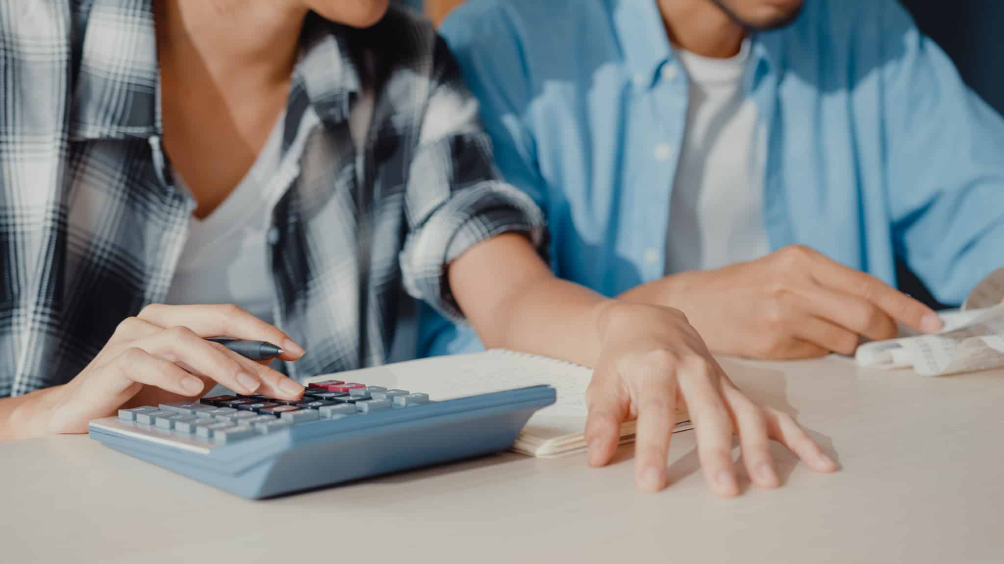 jovem casal confere faturas e documentos usando a máquina de calcular preparanod-se para ajustra o orçamento em tempos de crise financeira