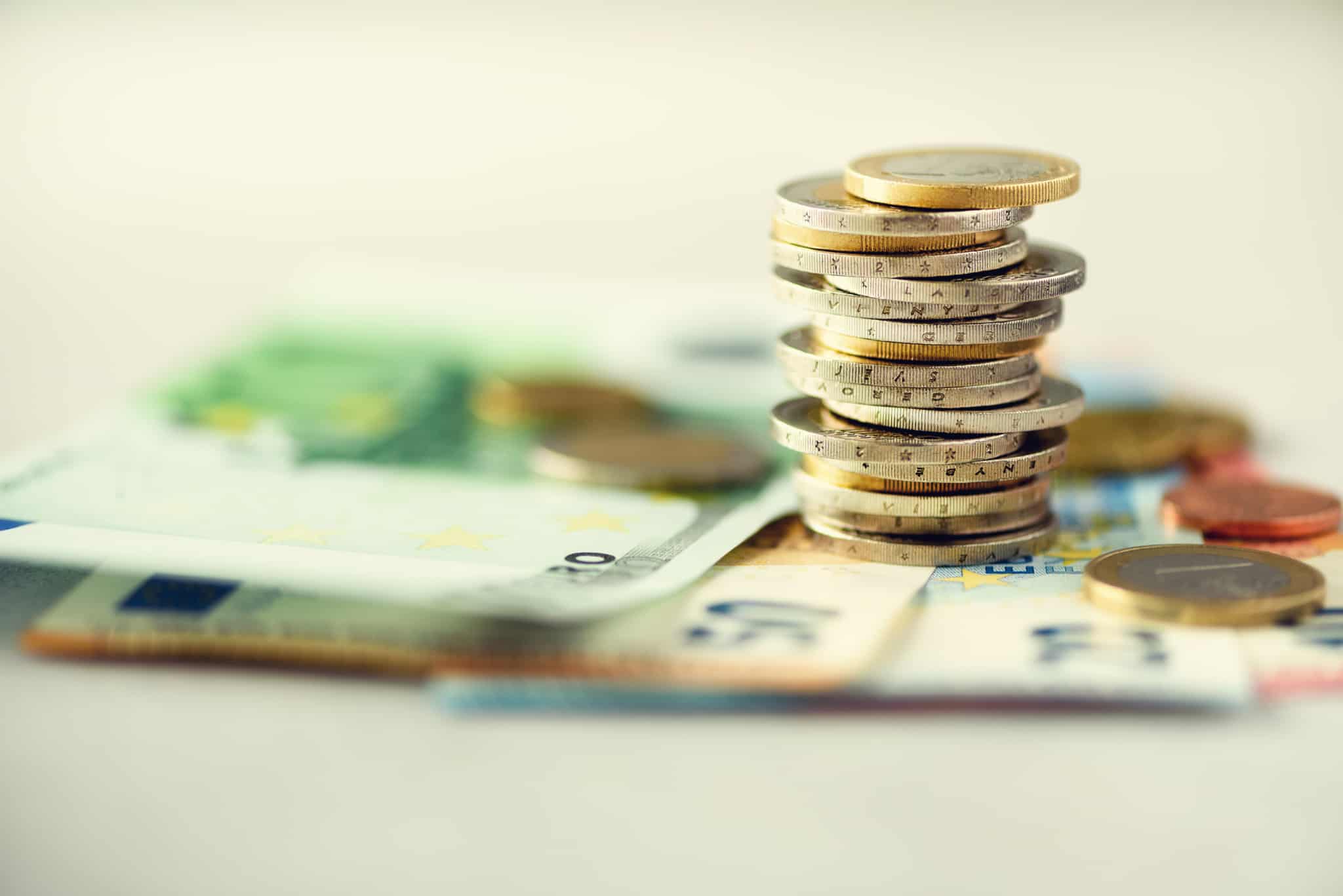 Notas de euro em cima de uma mesa, com um monte de moedas empilhadas