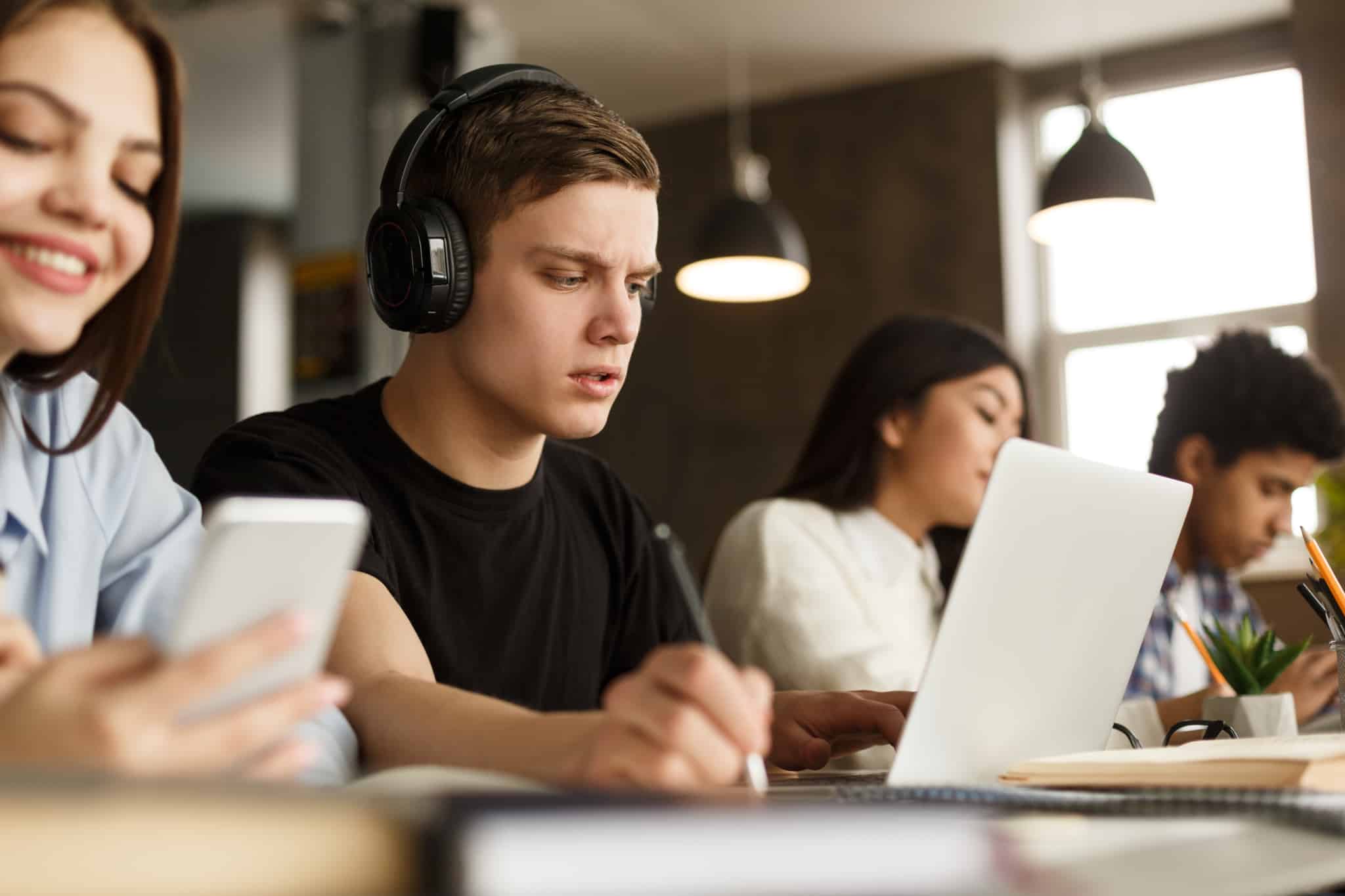 Alunos sentados numa secretária com computadores e telemóveis à frente numa sala de mestrado/pós-graduação