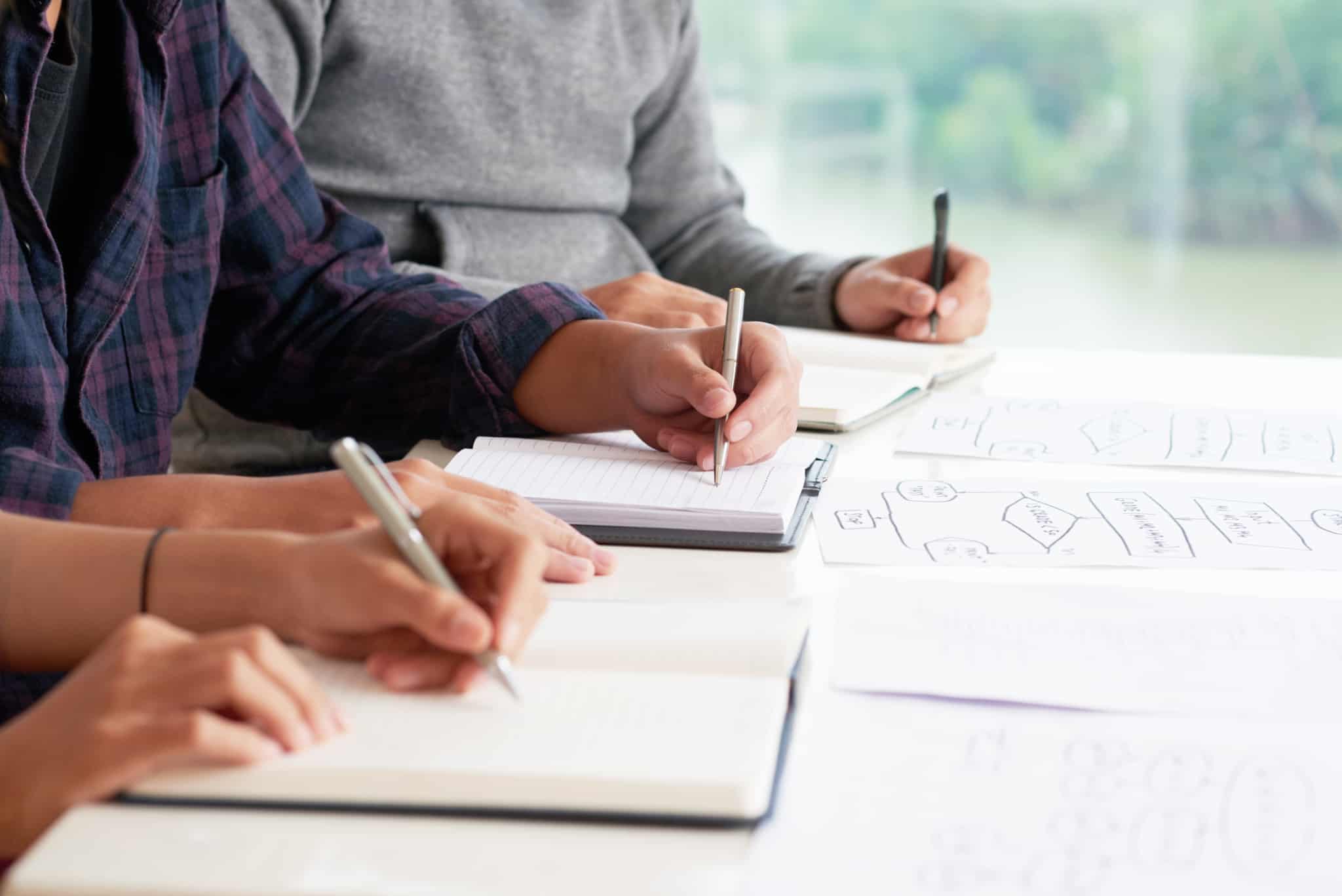 Estudantes fazem exercícios num caderno, enquanto estudam em conjunto
