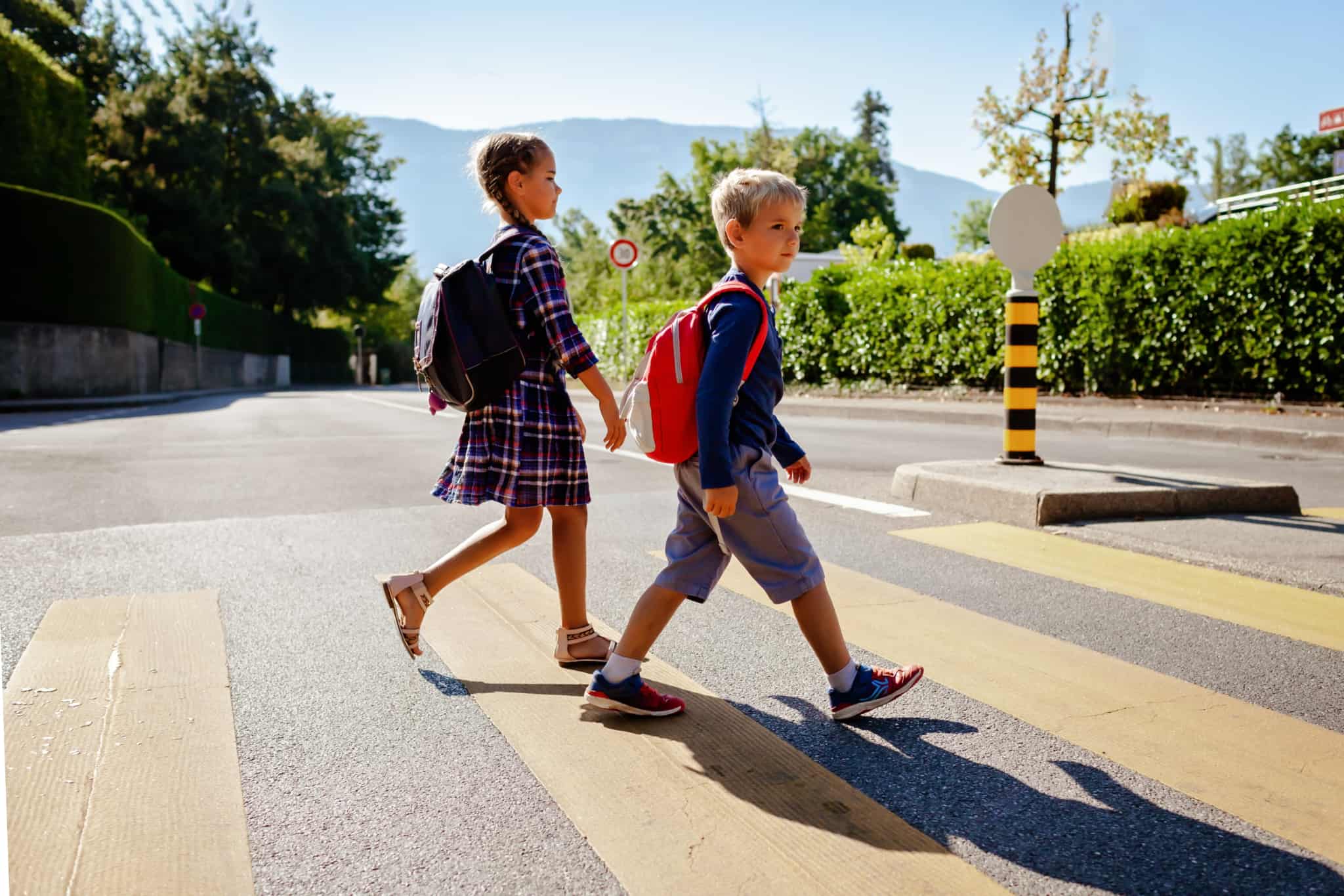 Duas crianças, um rapaz e uma rapariga, a passar a estrada de mochila às costas