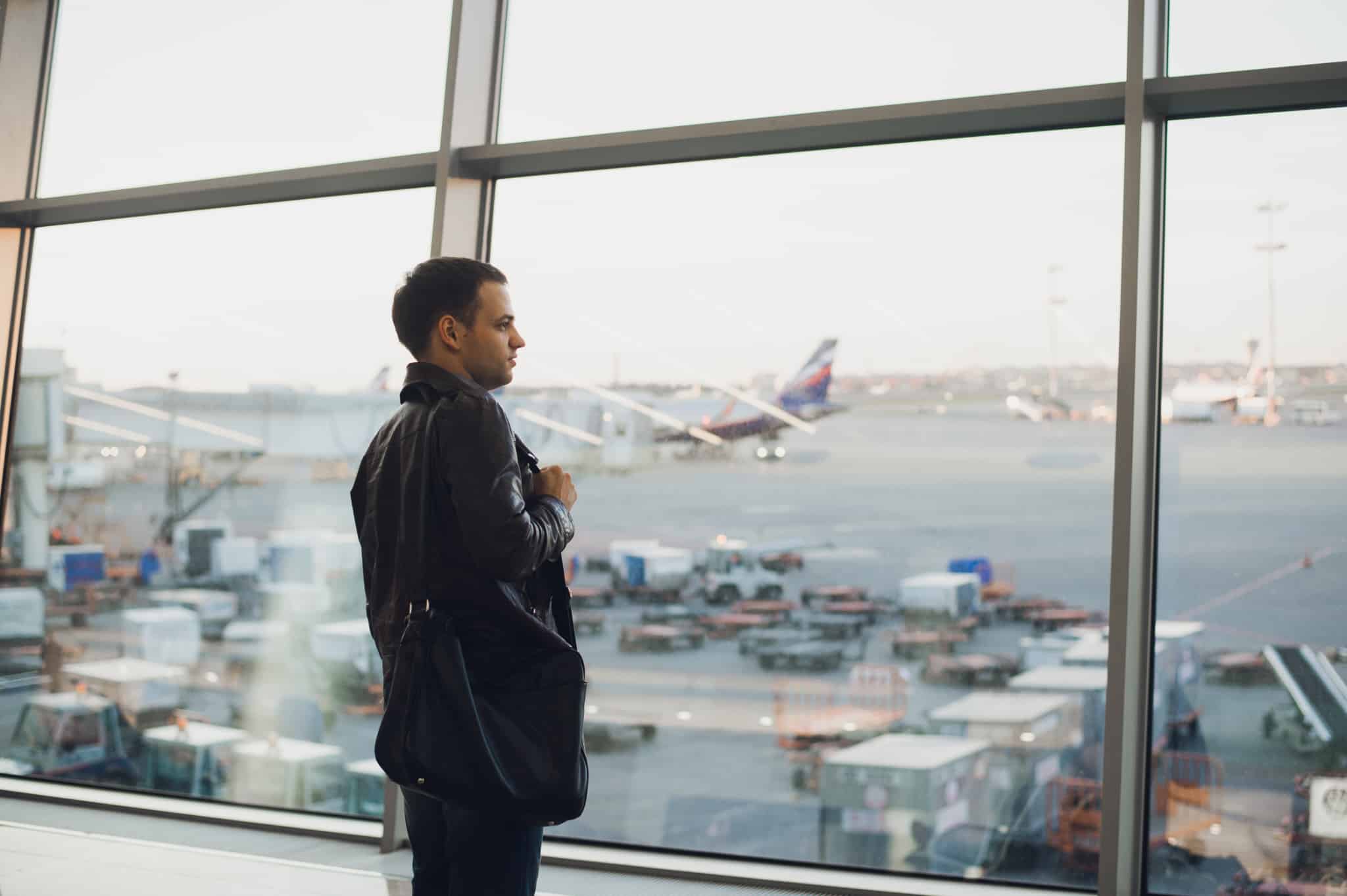 jovem rapaz junto a grande janela de aeroporto a contemplar a pista enquanto espera para resolver problemas com voo