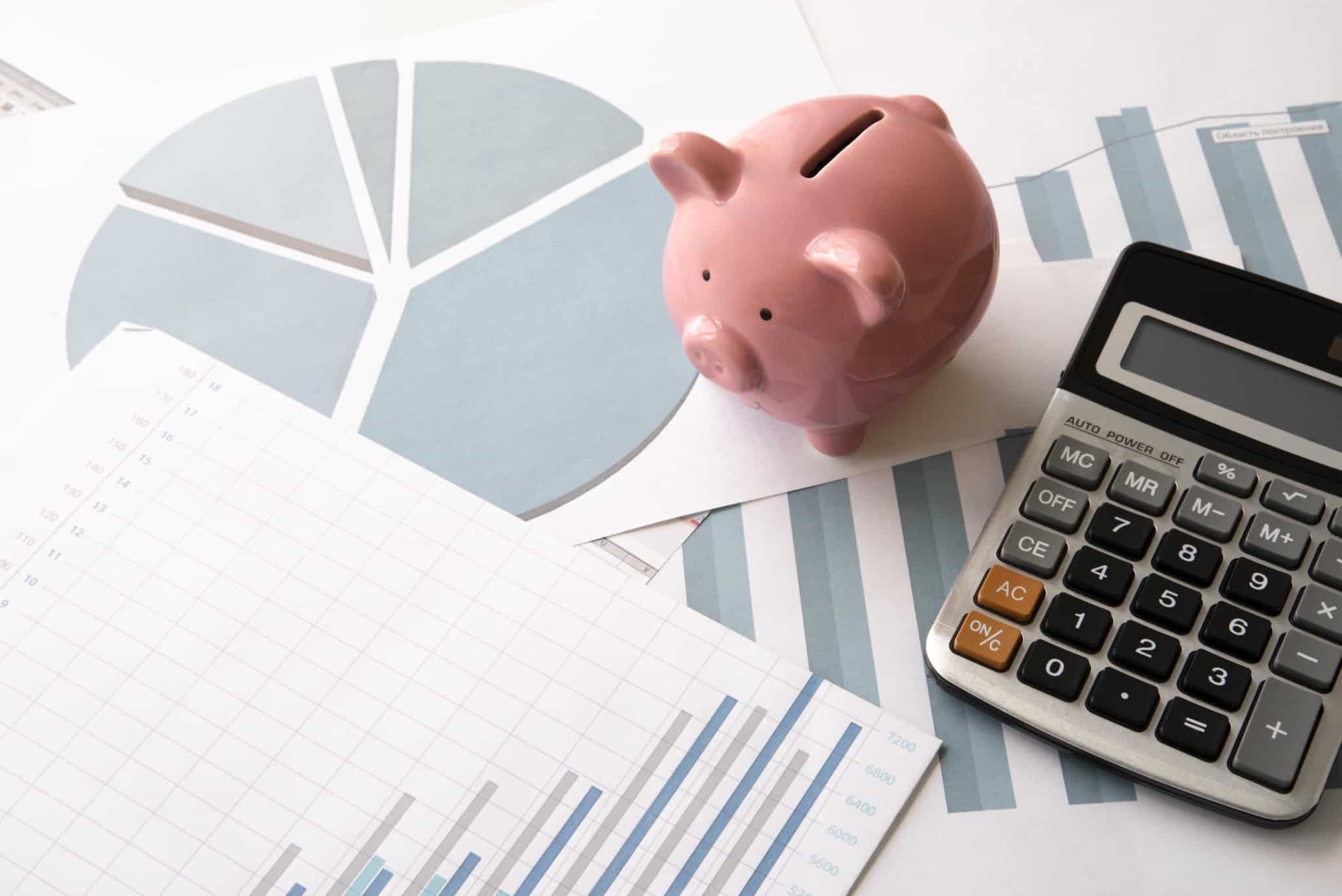 seguros de cpaitalização refletem a poupança , representada na imagem pelo porquinho mealheiro que está rodeado de documentos com gráficos e uma calculadora
