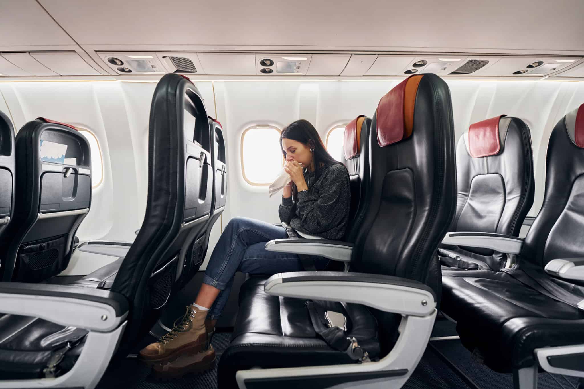 jovem mulher sentada no interior de um avião, a assoar-se e visivelmente doente, mas é portadora do Cartão Europeu de Seguro de Doença