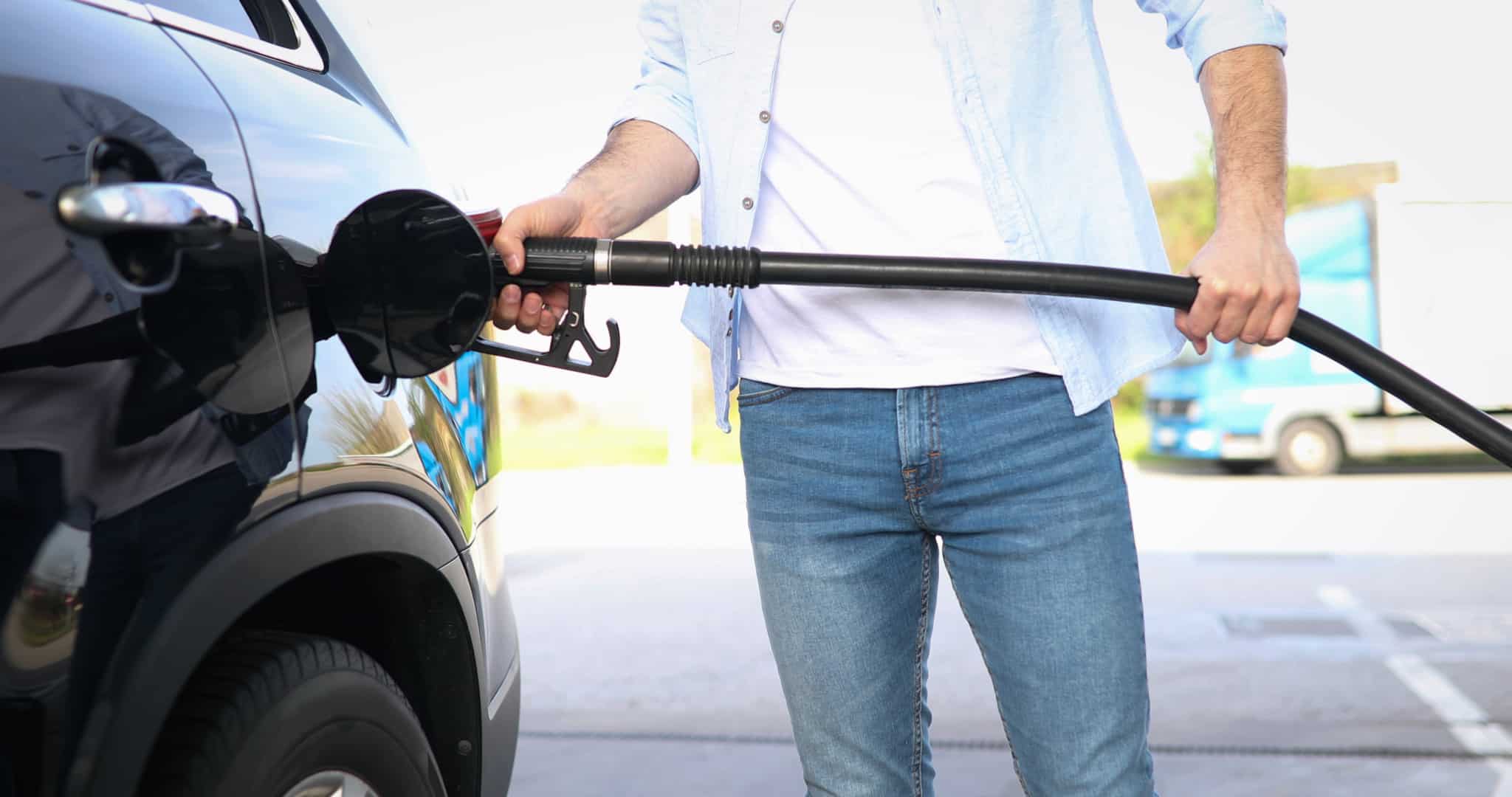 jovem homem a abastecer o carro na bomba de gasolina, optando entre combustível aditivado ou simples, de forma a conseguir poupar em tempos de grandes aumentos dos preços