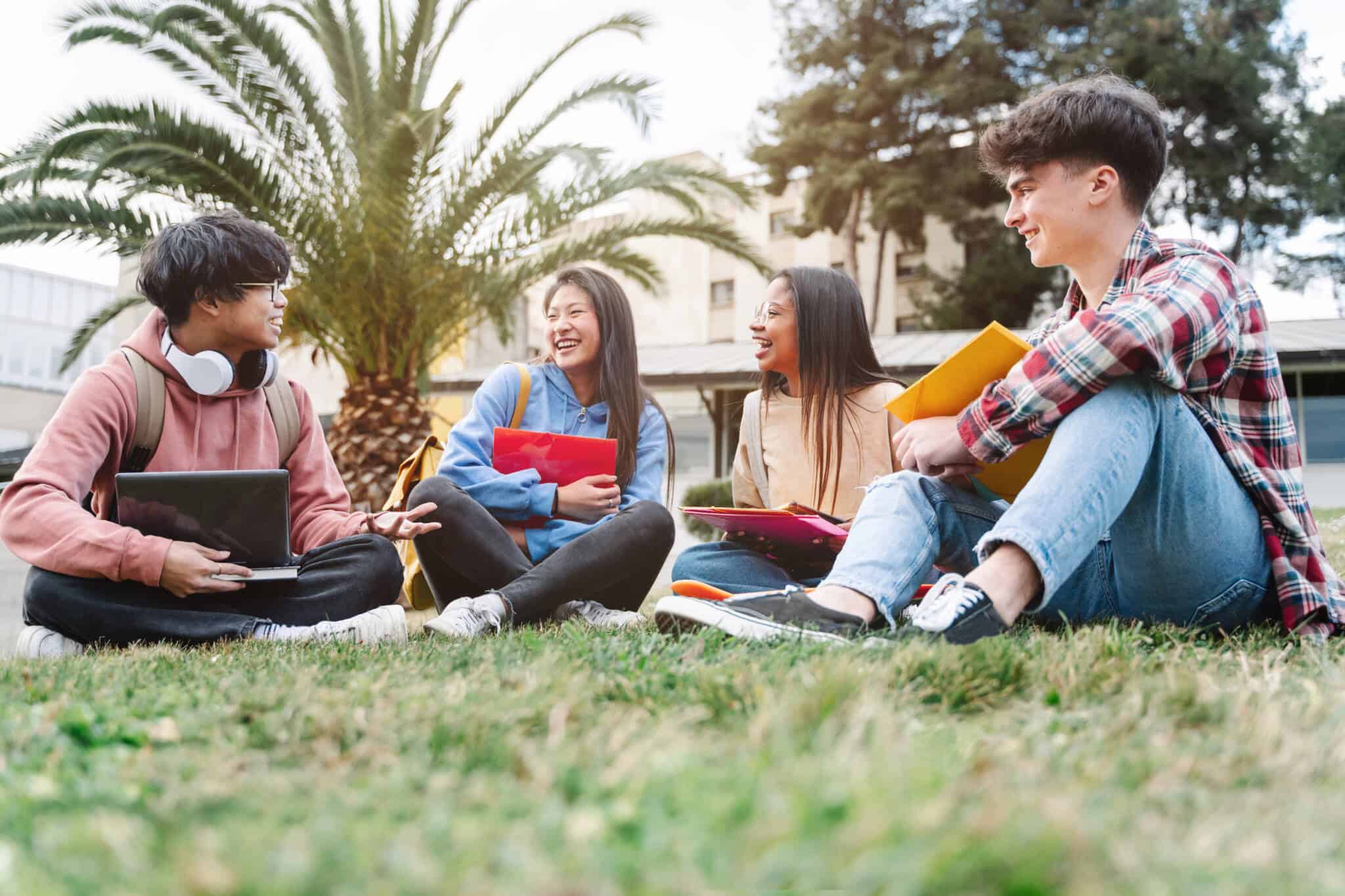 grupo de jovens universitários, sentados na relva de um campus universitário, oriundos de diversos destinos e raças, convivem no intercâmbio académico