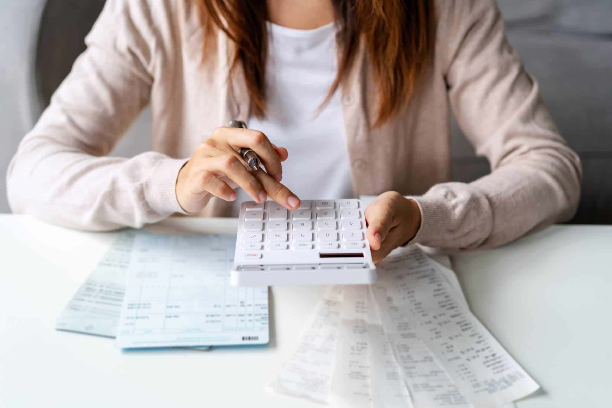 jovem mulher a usar a calculadora para reduzir orçamento mensal, analisando a mesa cheia de faturas