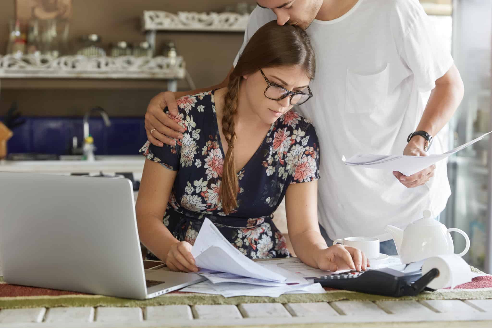 Casal sentado à mesa com computador e papéis à frente a analisar e reequilibrar contas pós férias