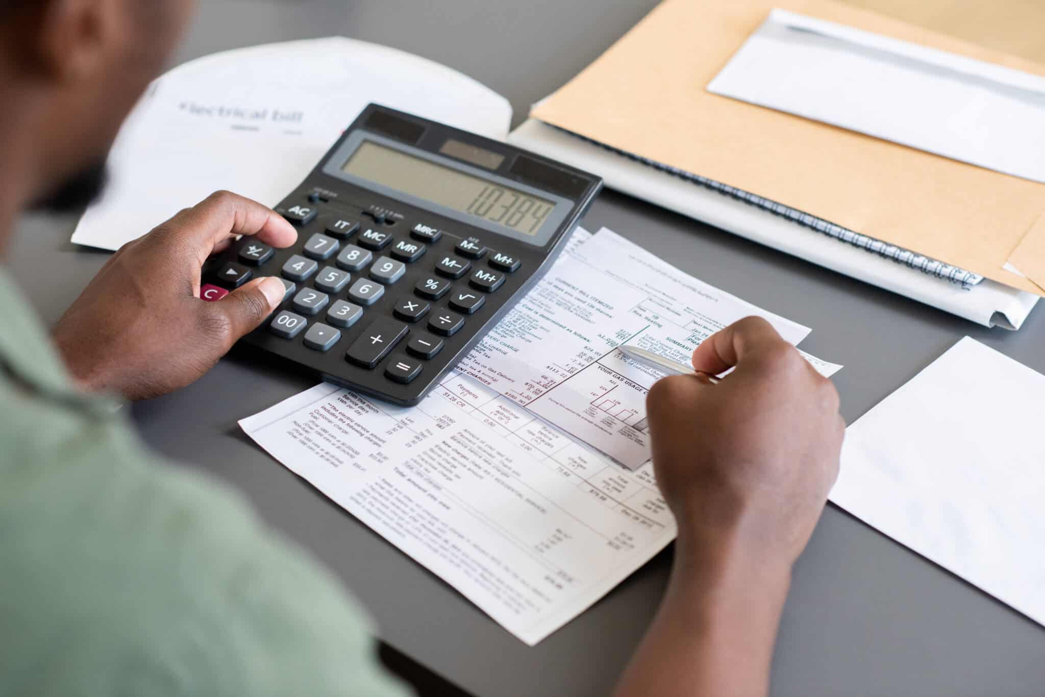 mão de jovem a consultar faturas e somar os valores na calculadora, de forma a tomar decisões financeiras importantes