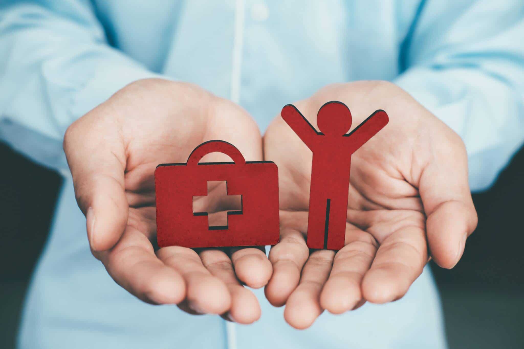 Mãos de homem a segurar peças madeira mala de emergência e boneco a simbolizar coberturas de seguro de vida