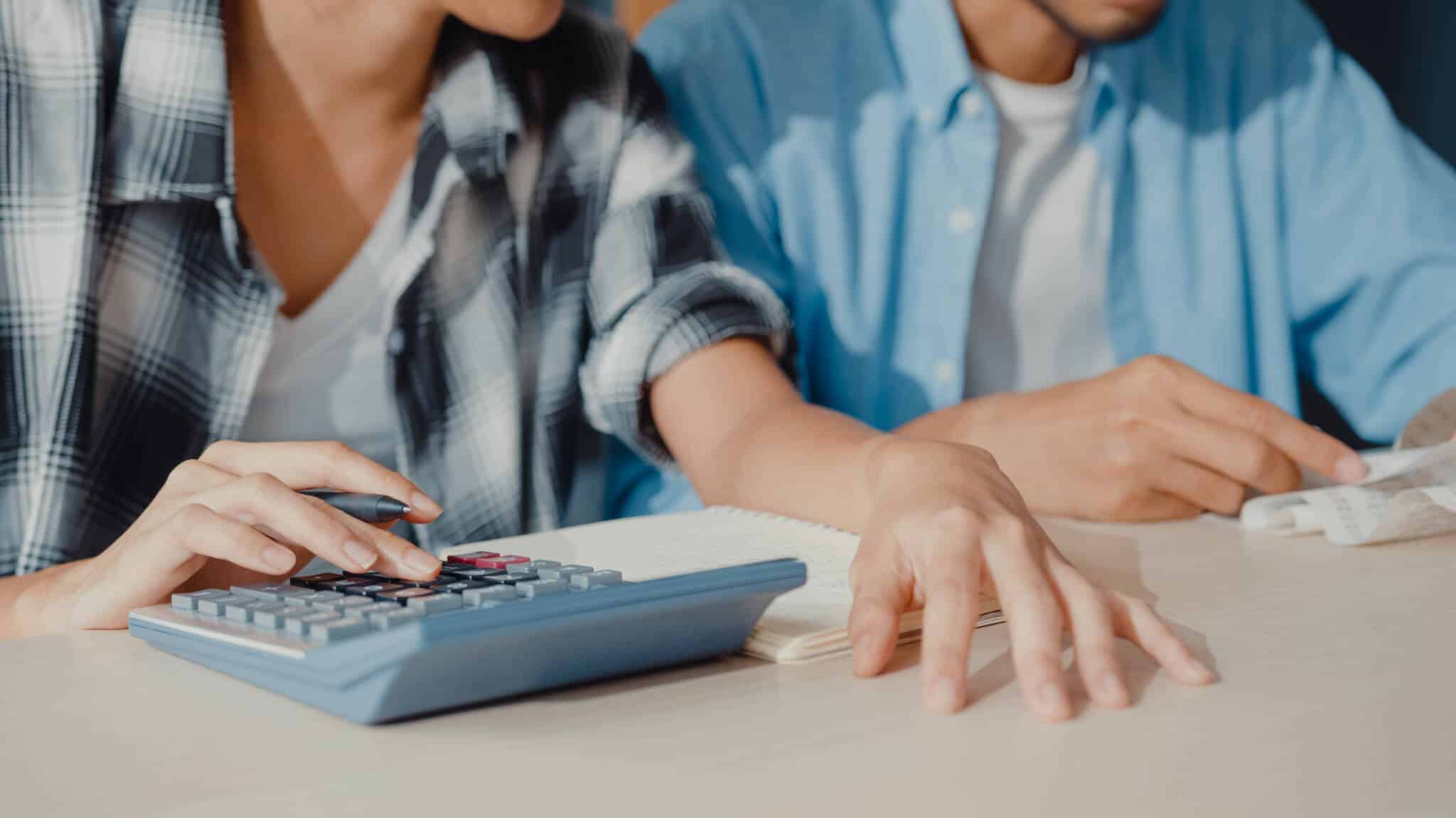 jovem casal conulta faturas e recorrer a calculadora para analisar e somar as despesas, inclusive as inesperadas para ajustar o orçamento