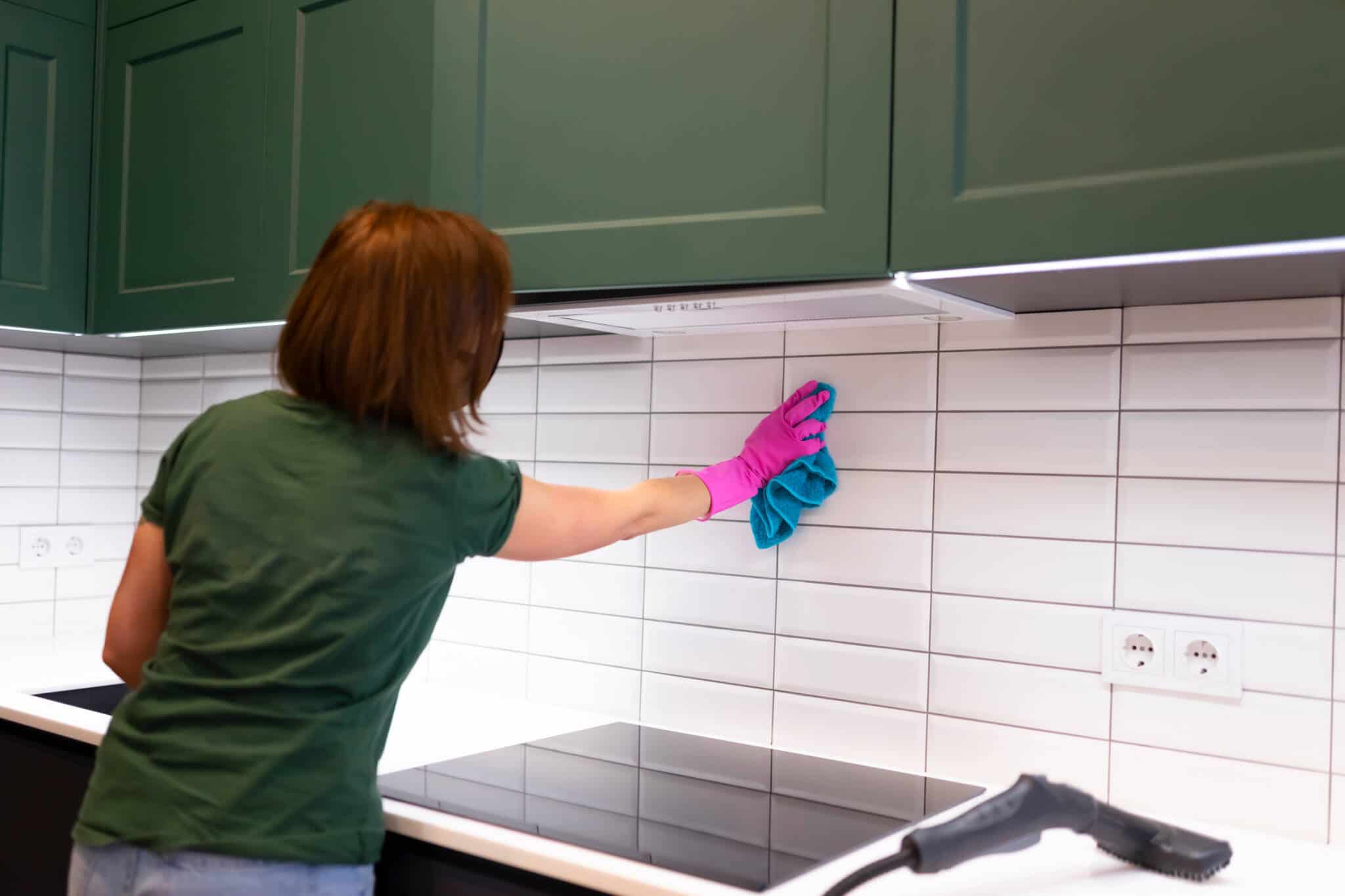 jovem mulher, empregada doméstica, limpa os azulejos na cozinha com pano e máquina de limpeza
