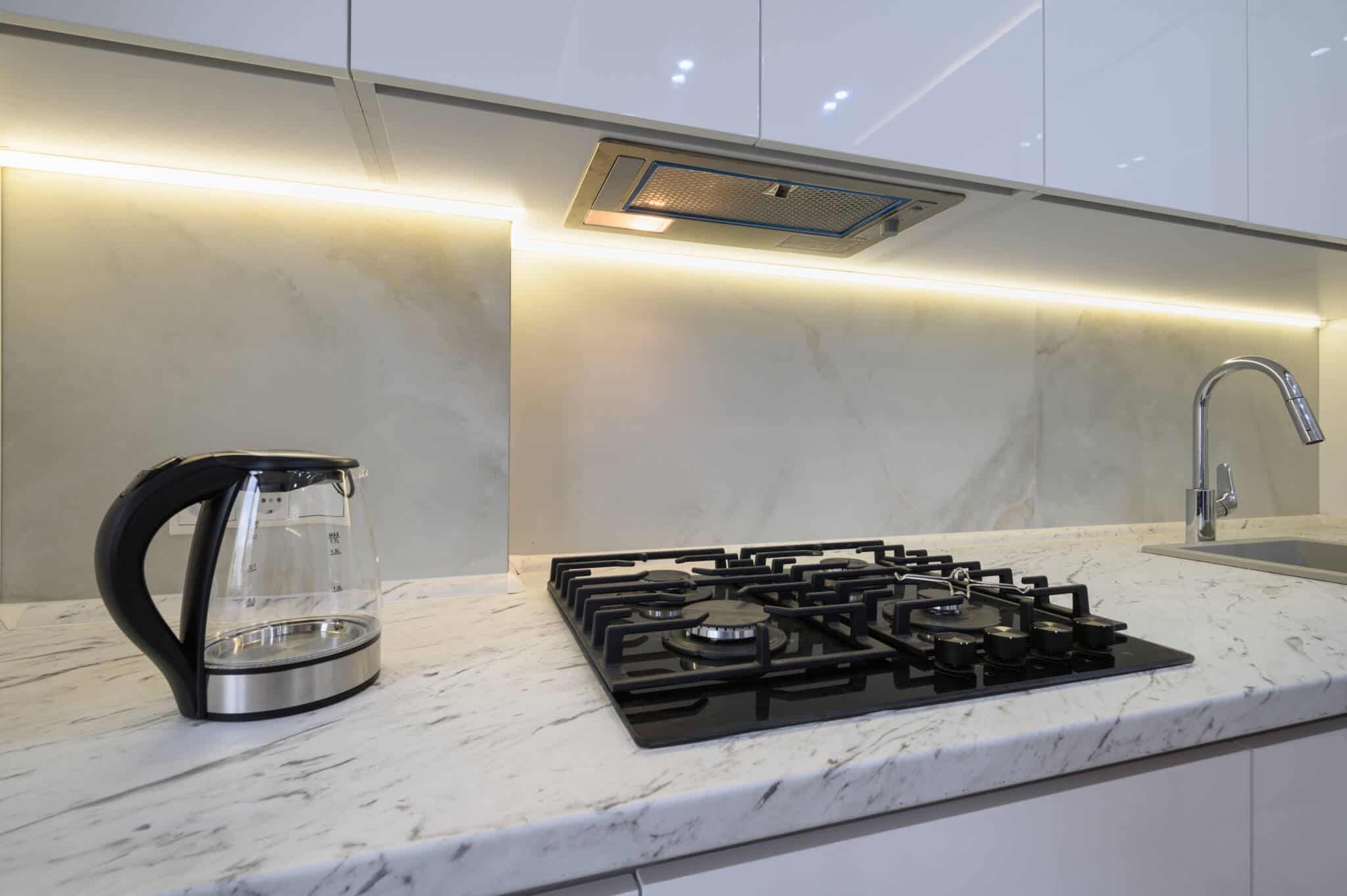 gás e eletricidade e a possibilidade de voltar ao mercado regulado ilustrada com uma bancada de cozinha, branca e moderna, com fogão a gás e uma forte iluminação no móvel superior