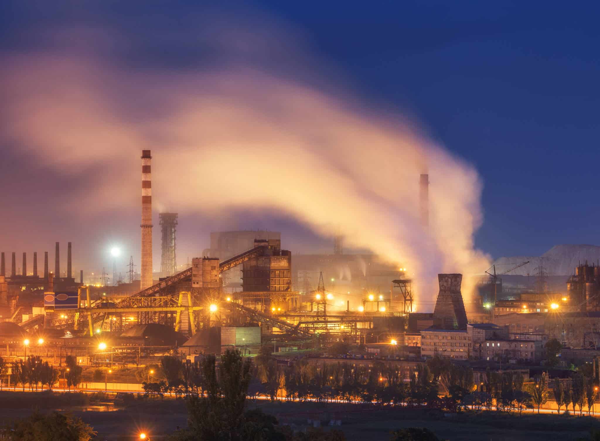 mercado do carbono ilustrado com imagem de uma metalurgica em pleno funcionamento, durante a noite, com gfrande emissão de gases para a atmosfera