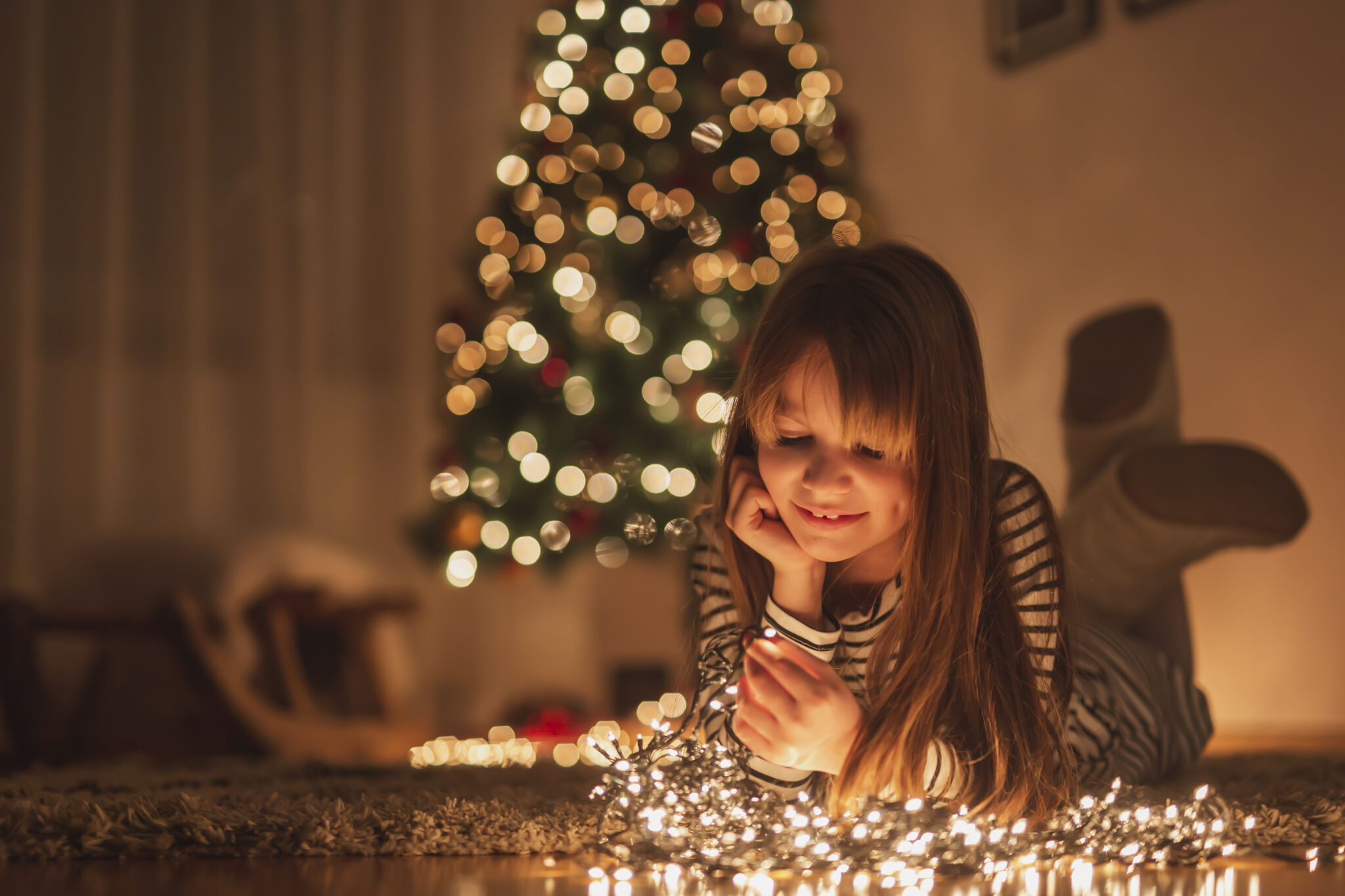 Criança rapariga deitada no chão com luzes de natal e árvore de natal por trás