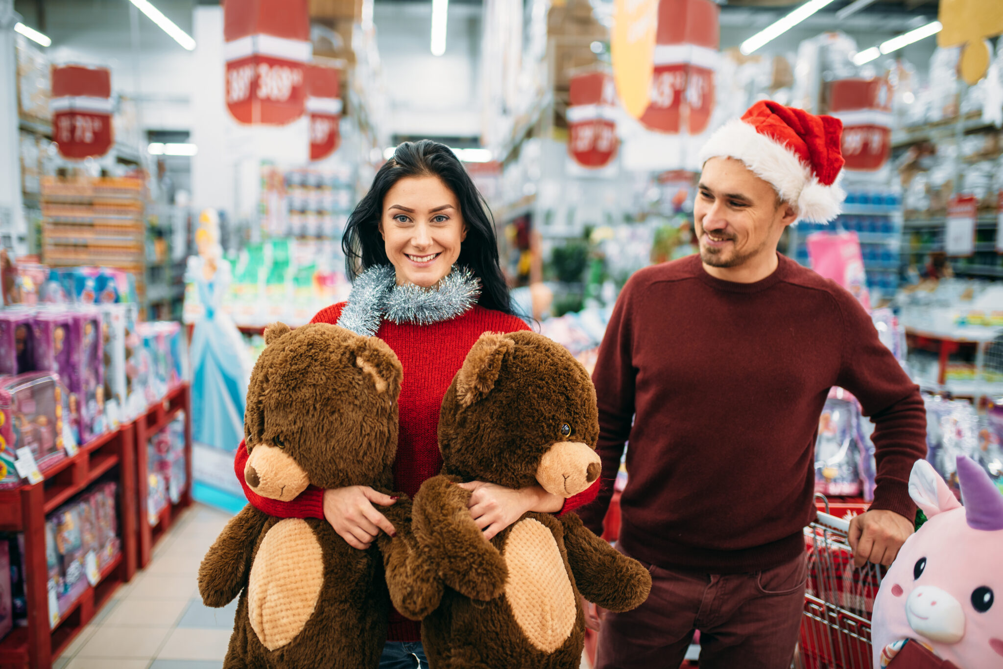 jovem casal às compras numa grande superfície comercial a aproveitar promoções em brinquedos, transportam dois ursos gigantes de peluche