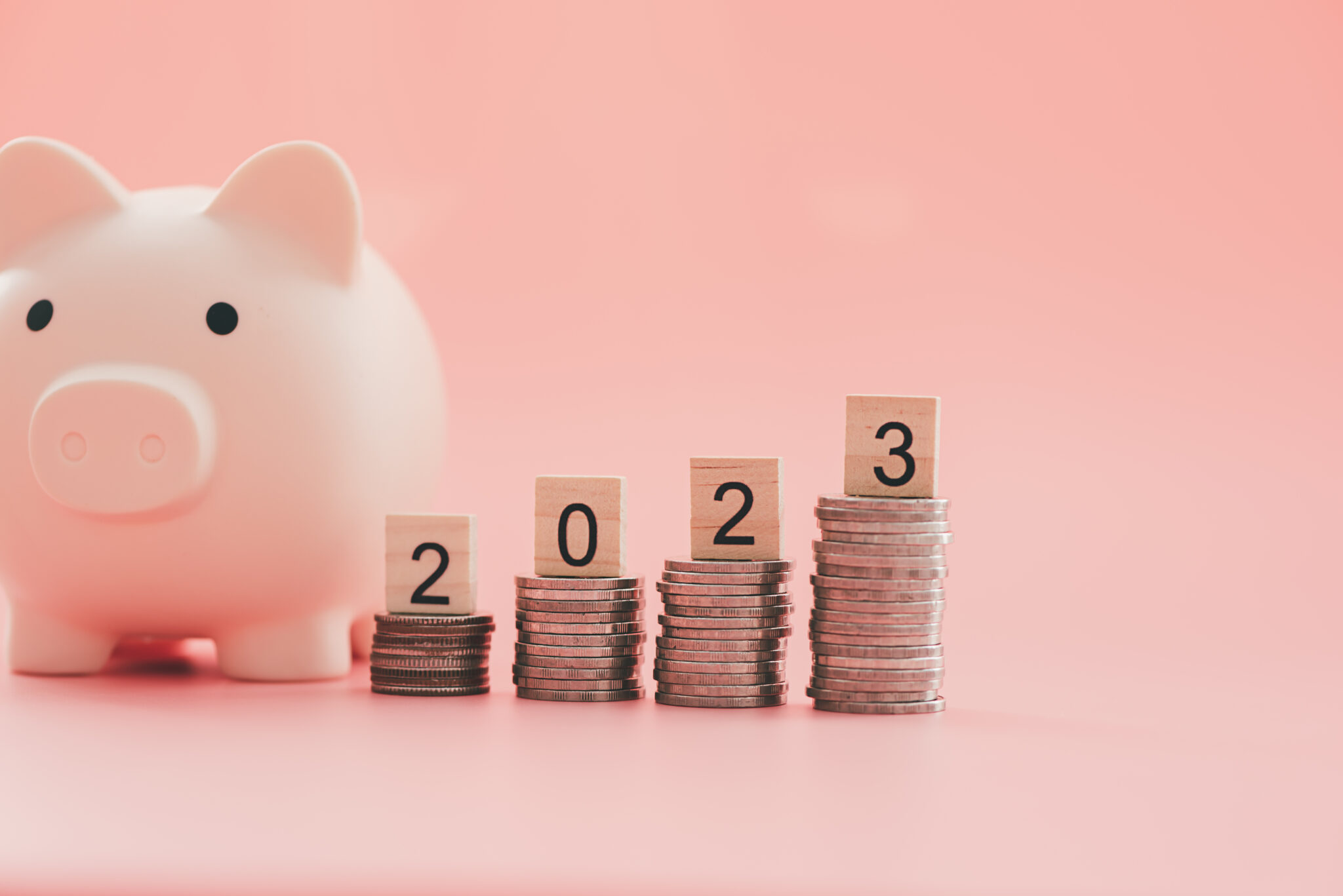 2023 e dicas de poupança para todo o ano, um tema ilustrado com um porquinho mealheiro rosa, em fundo rosa, junto a pilhas de moedas em crescendo com os números do novo ano em casa uma