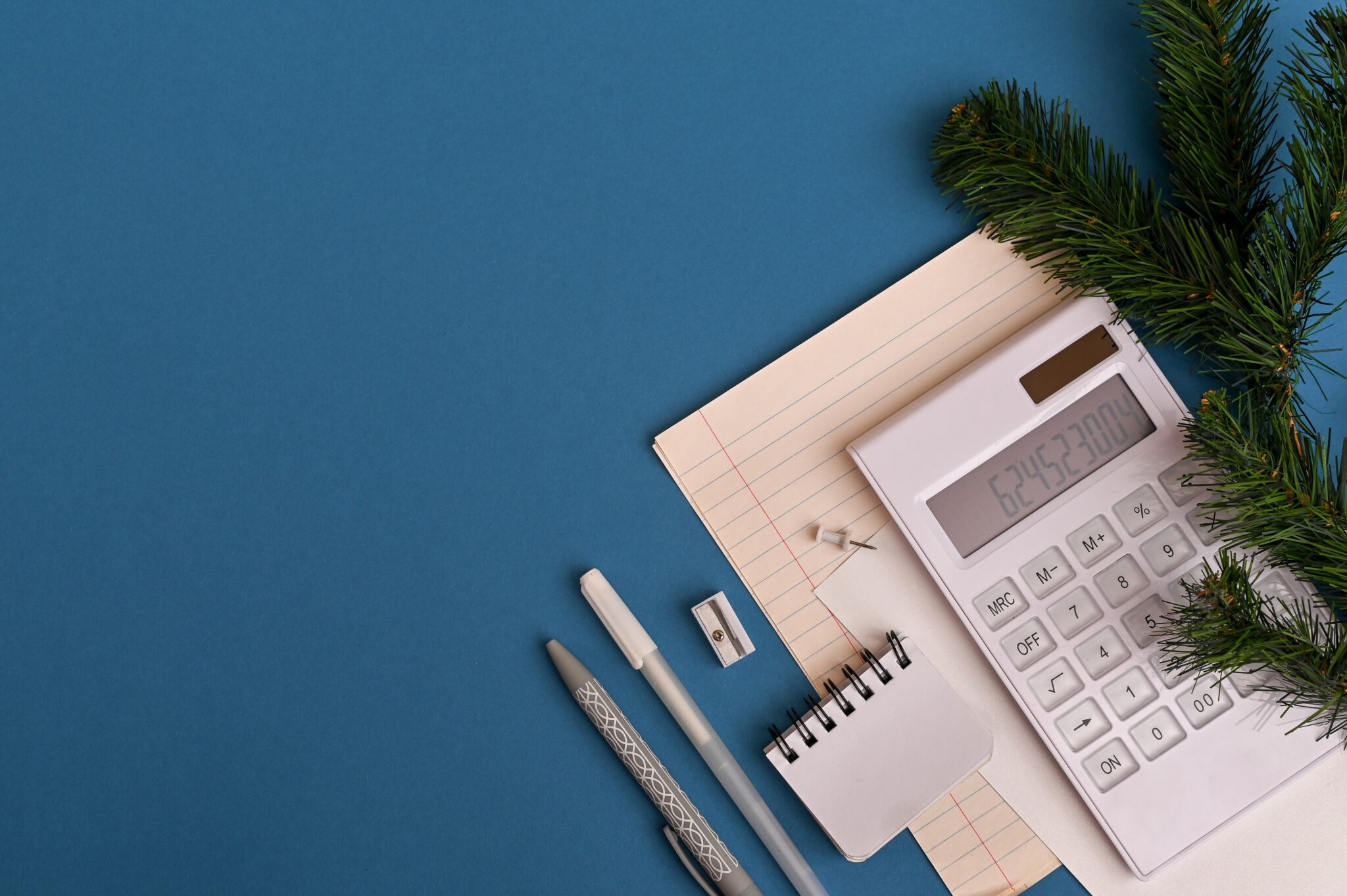 Plano azul com folhas de papel, caderno, lápis e afia com calculadora a simbolizar contas e entrar em 2023 com carteira arrumada