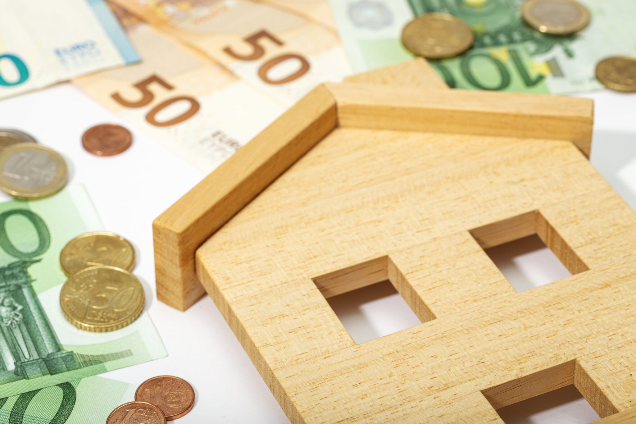 Casa de brincar madeira por cima de notas e moedas euros representando rendas em 2023