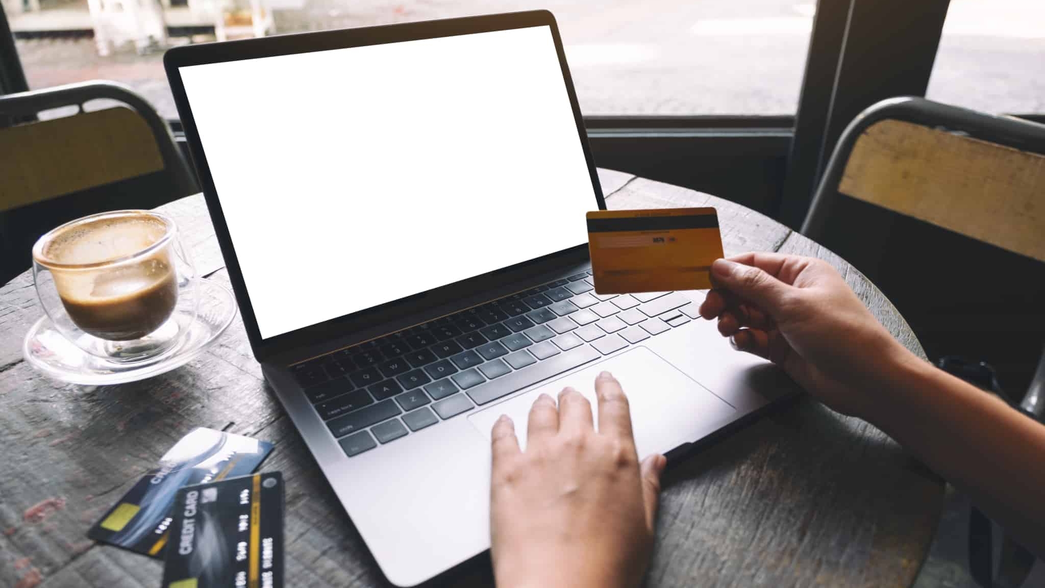 um ecrã de computador com mãos de homem a segurar cartão de crédito e monte de cartões de crédito ao lado na mesa