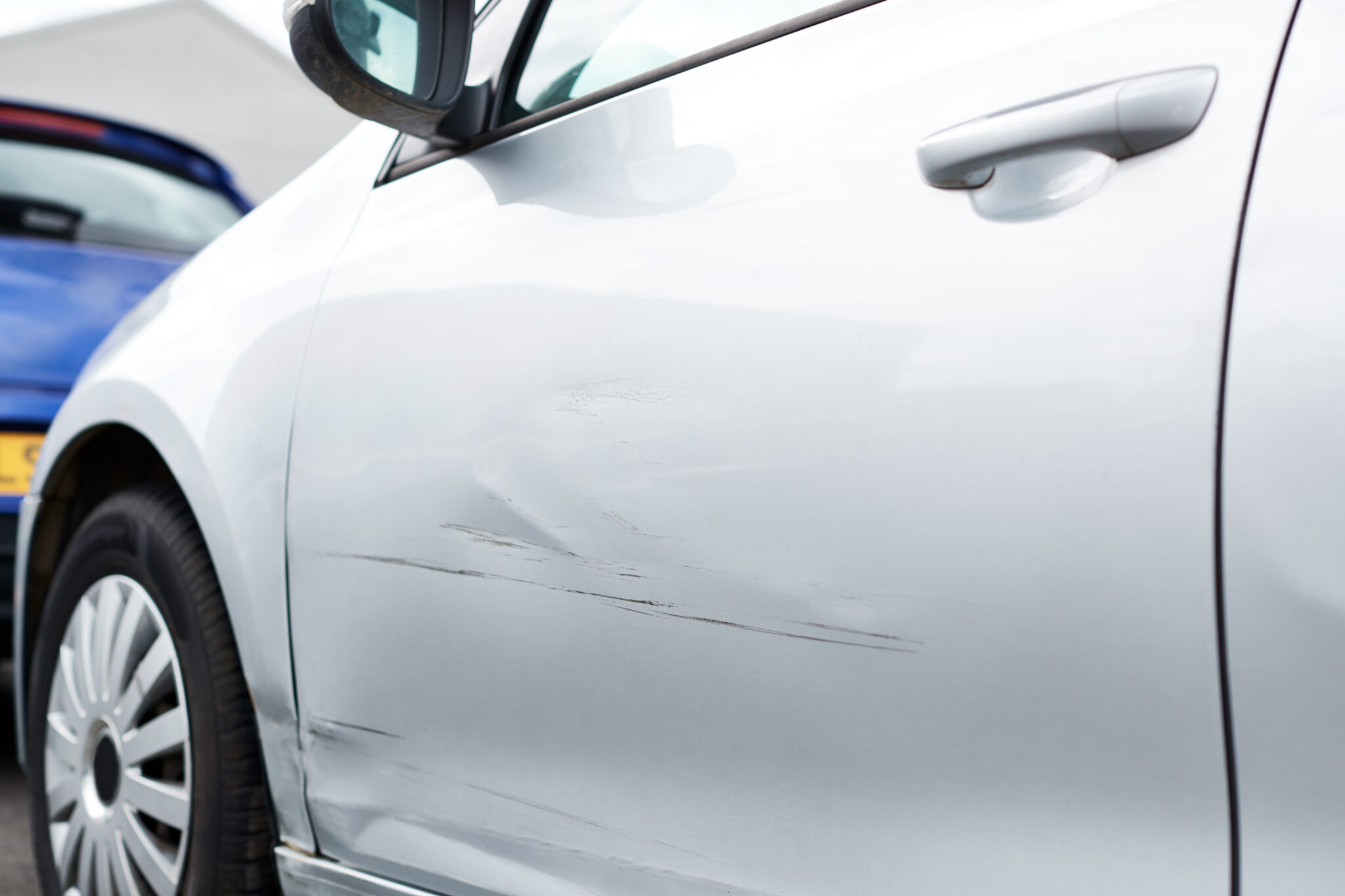 lateral de um carro riscado, branco, em mau estado, ilustrando o q pode ser feito nestas situações