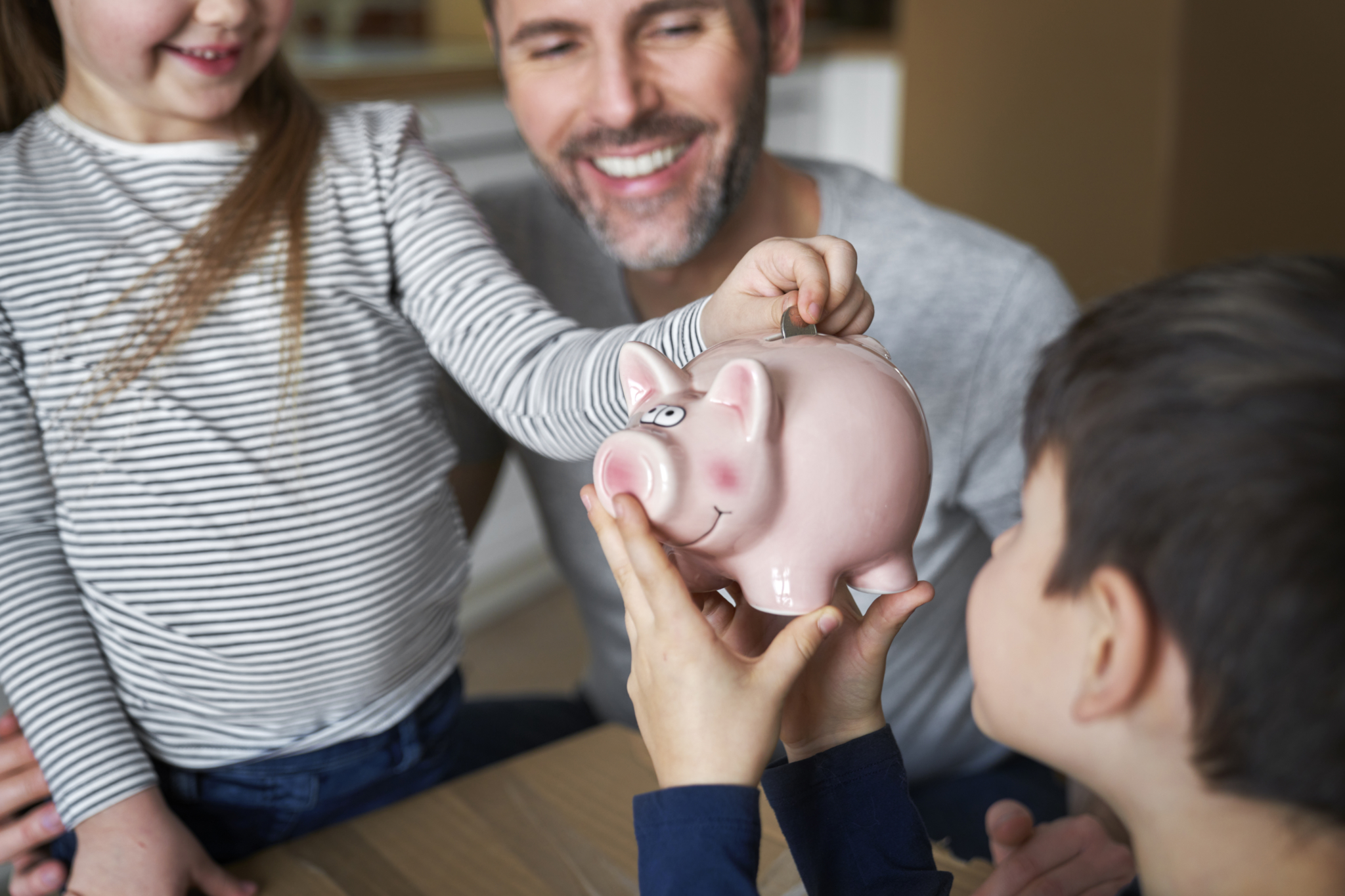 pai com os filhos e um porquinho mealheiro a mostrar como é possível poupar em tempos de crise