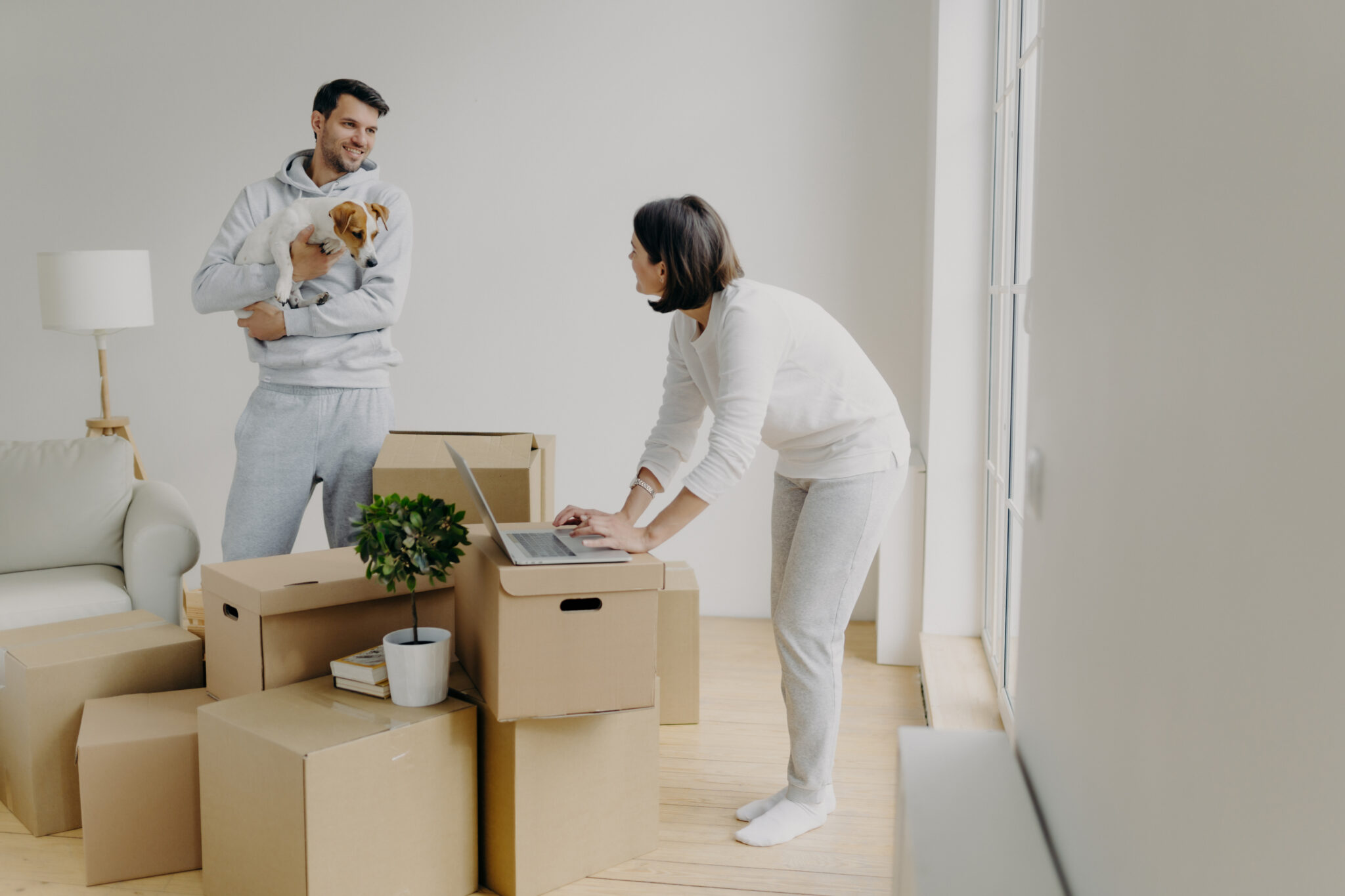casal a desfazer as caixas de mudança, com um cão ao colo, em abiente de felicidade pela decisão de comprar a casa certa