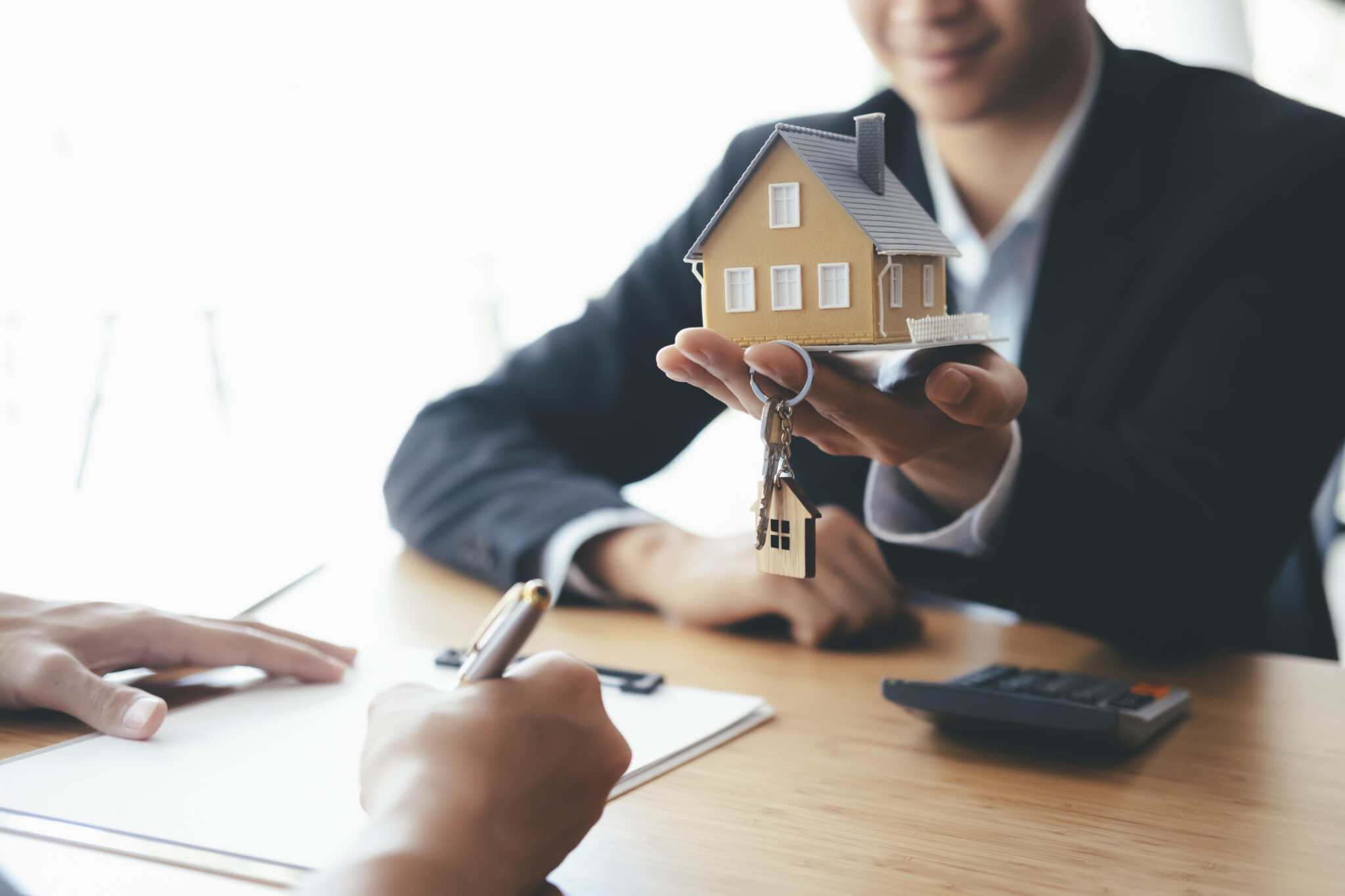 pessoa a segurar uma casa na mão e uma chave e outra a assinar um contrato depois dos novos apoios no crédito habitação
