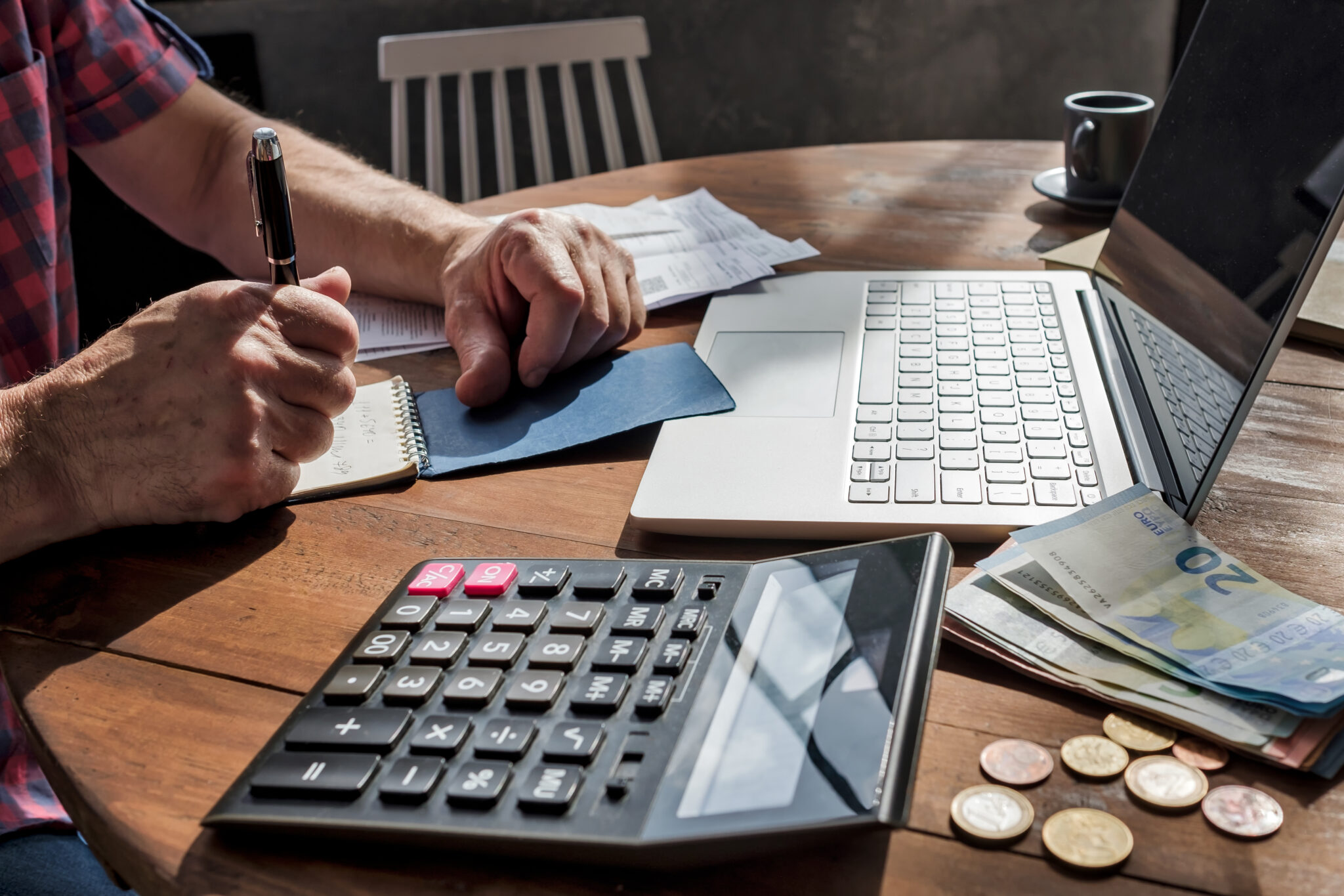 homem a fazer contas num bloco de notas, com a calculadora e o computador à frente para saber o valor do seu salário em 2023