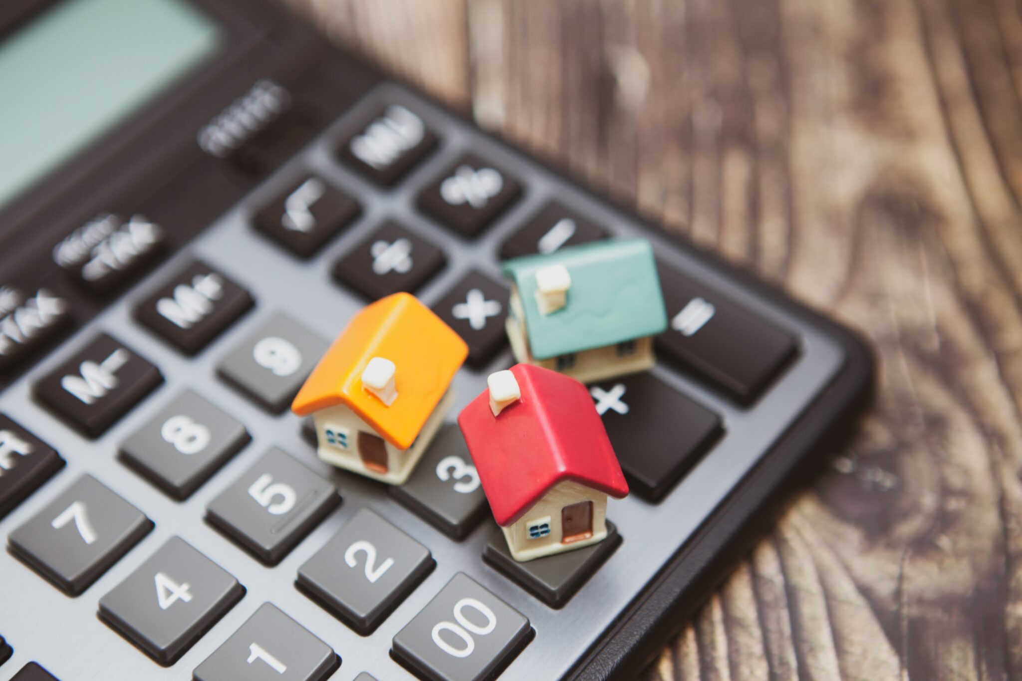 Calculadora com maquetes miniatura de três casas simbolizando taxa mista no crédito habitação