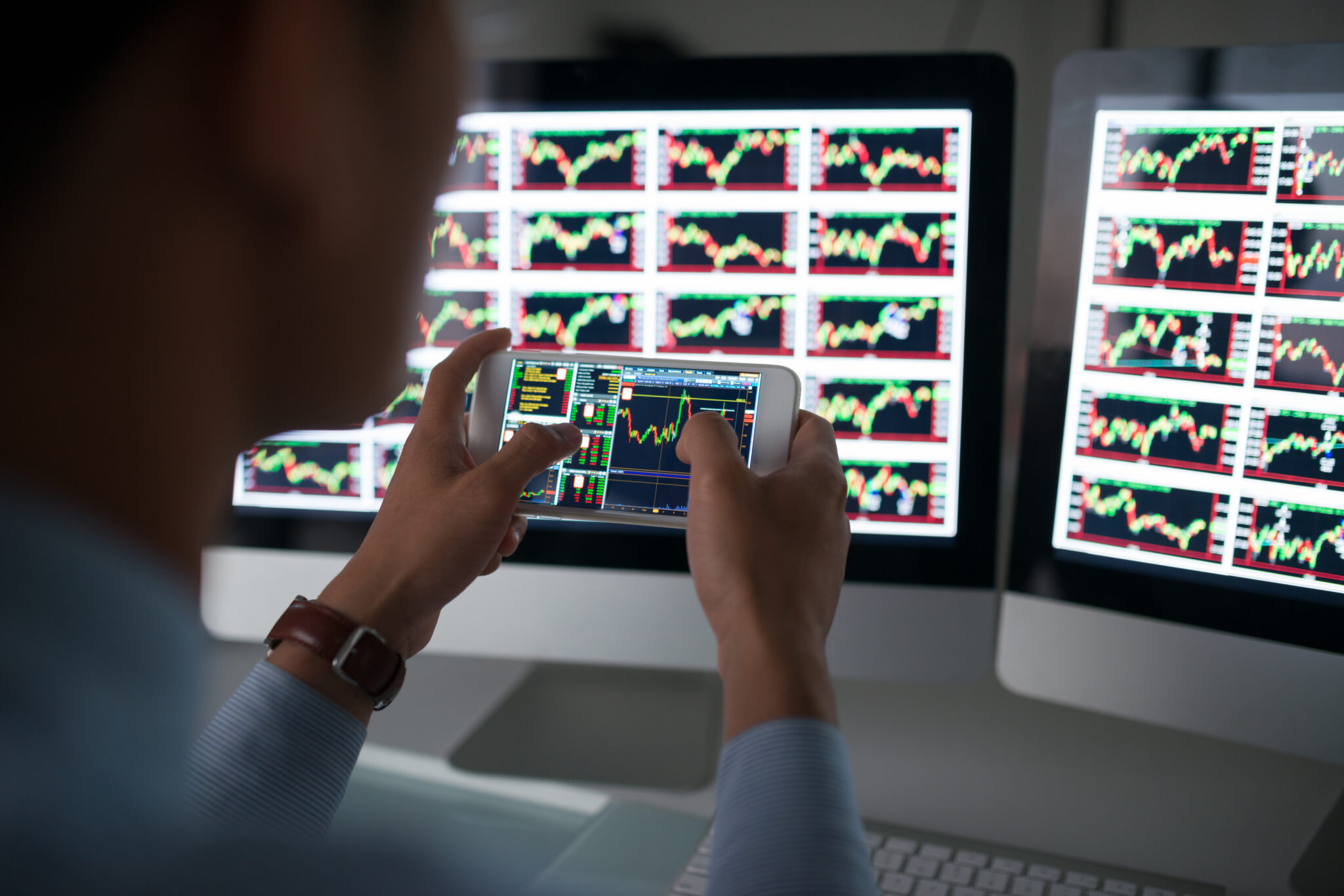 Investidor a analisar gráficos dos mercados no computador e smartphone