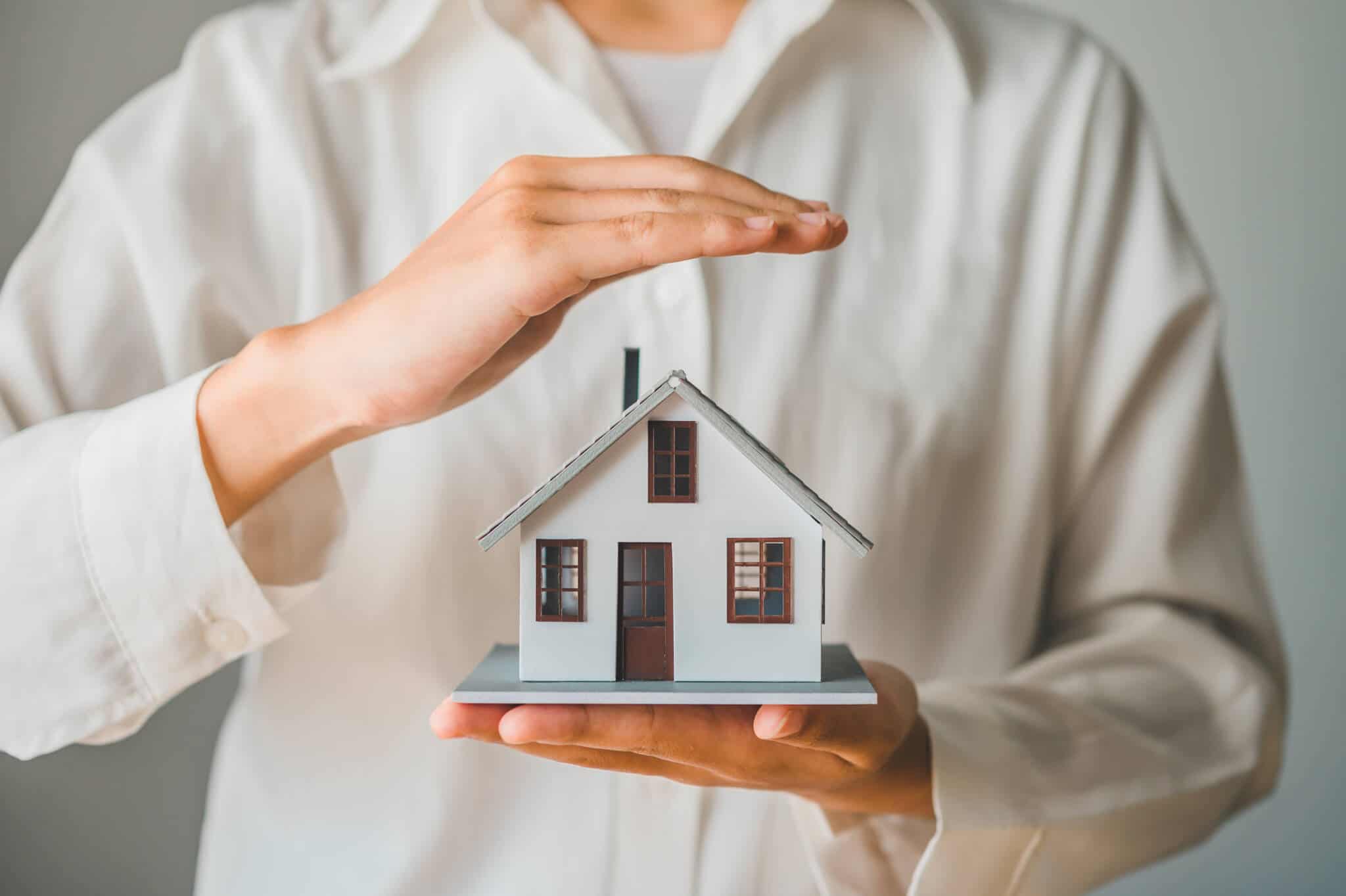 Pessoa a segurar maquete de casa numa mão e a proteger casa com a outra para simbolizar seguros