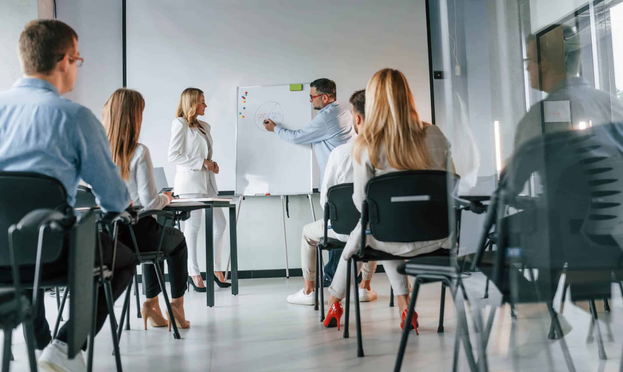 grupo de jovens, honens e mulhees, assistem a fomação lecionada por um casal, tratando-se de um cursos sobre finanças pessoais