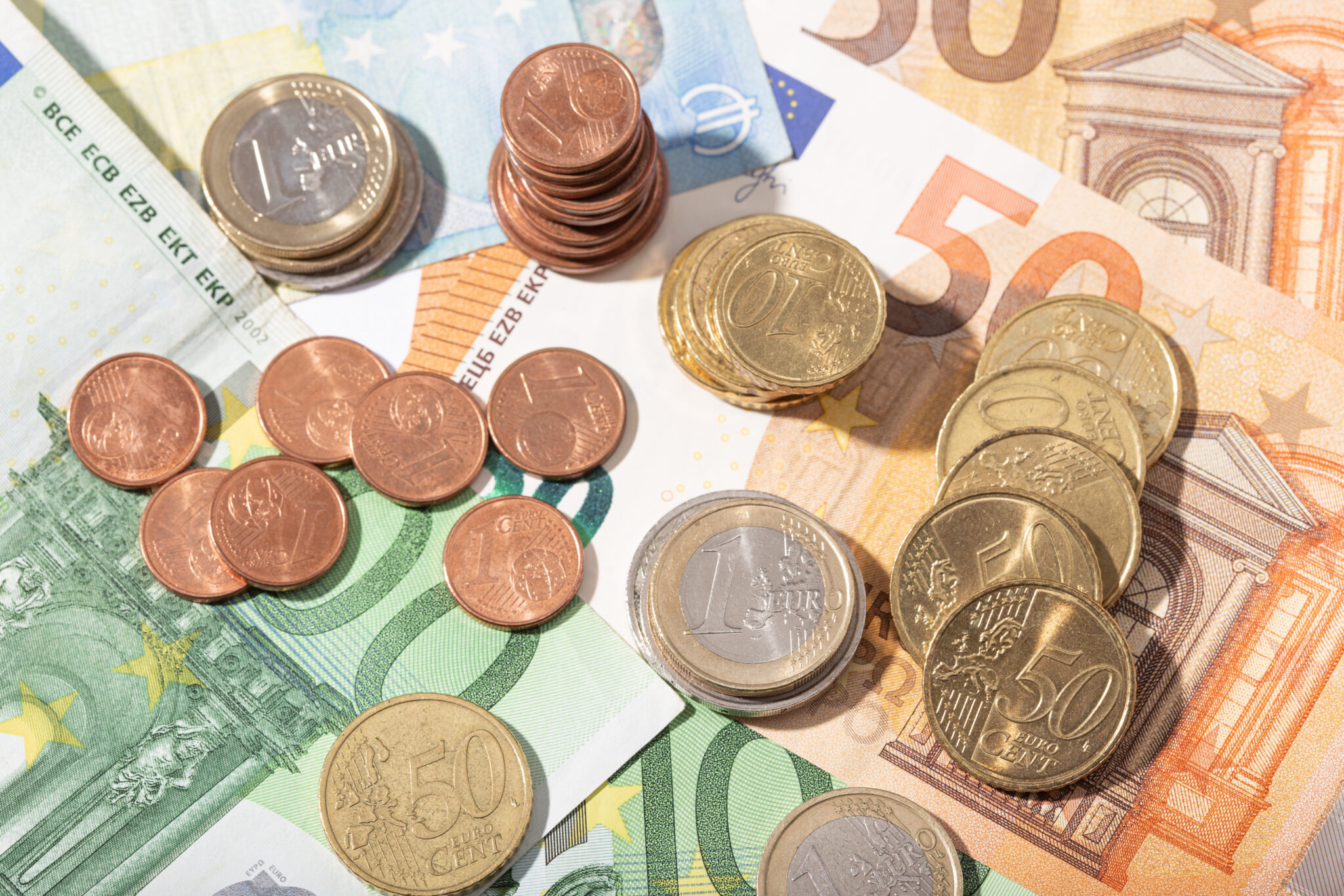 notas de euro espalhadas em cima da mesa, com várias moedas de euro sobrepostas
