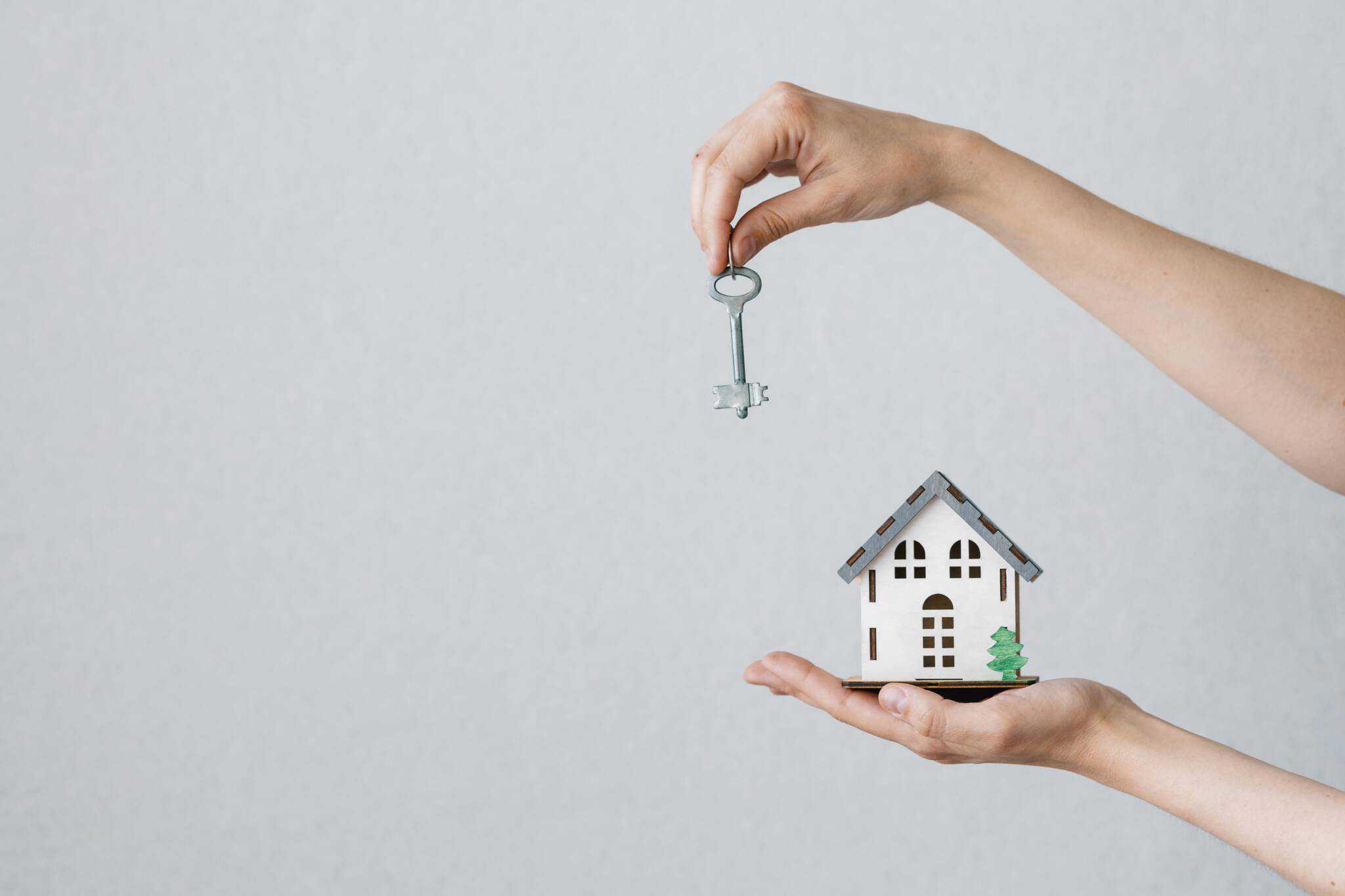Mãos a segurar maquete miniatura de casa e uma chave a vender casa