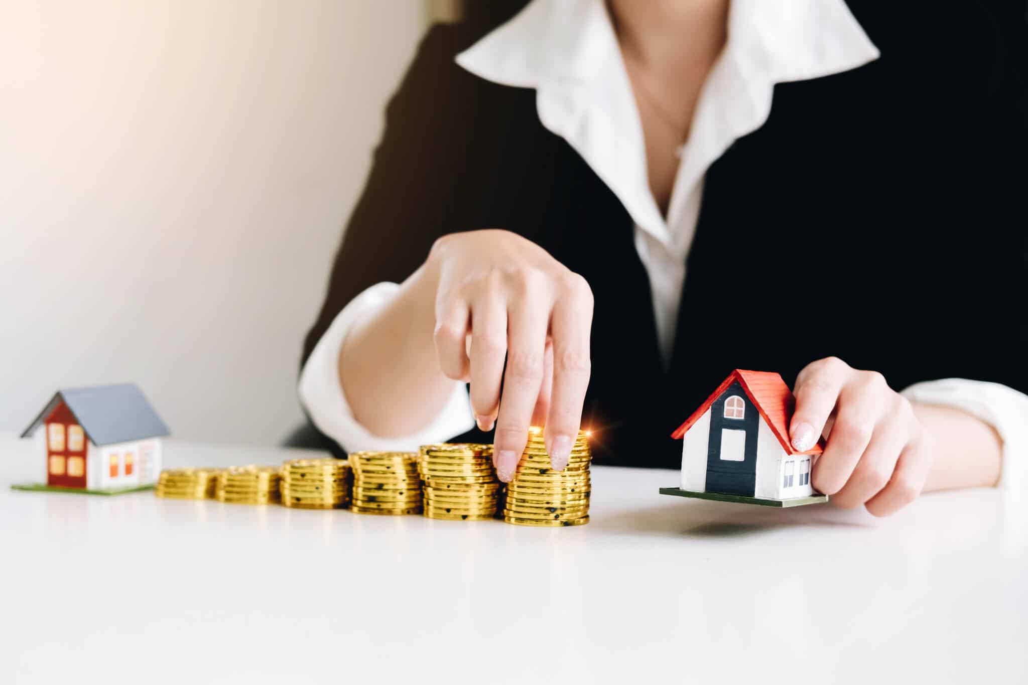 mulher com moedas na mão e uma casa em miniatura a ilustrar o aumento das prestações de crédito habitação em abril
