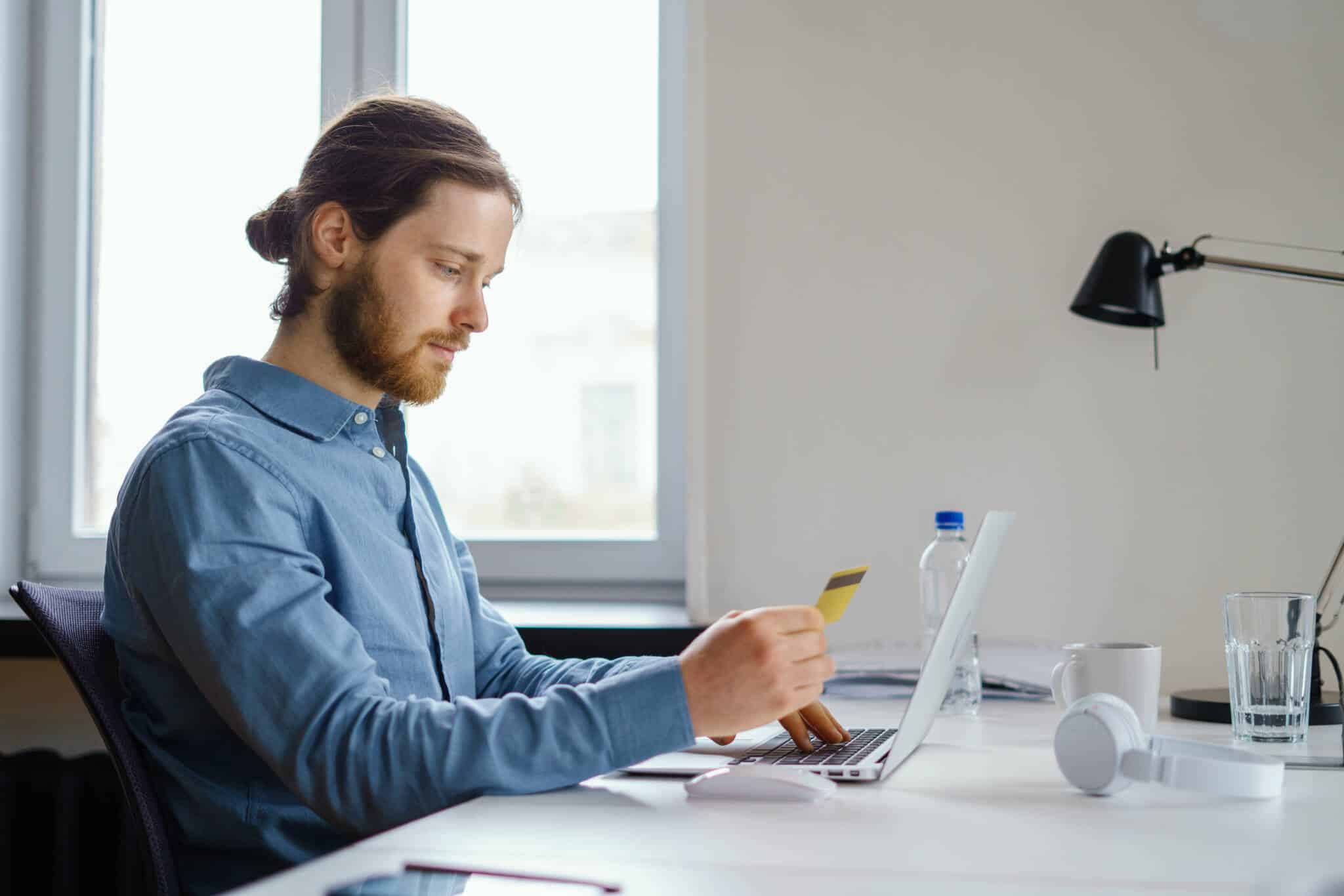 Homem com um cartão de crédito na mão frente ao computador a verificar as taxas máximas do crédito ao consumo aumentam no 2ºtrimestre de 2023