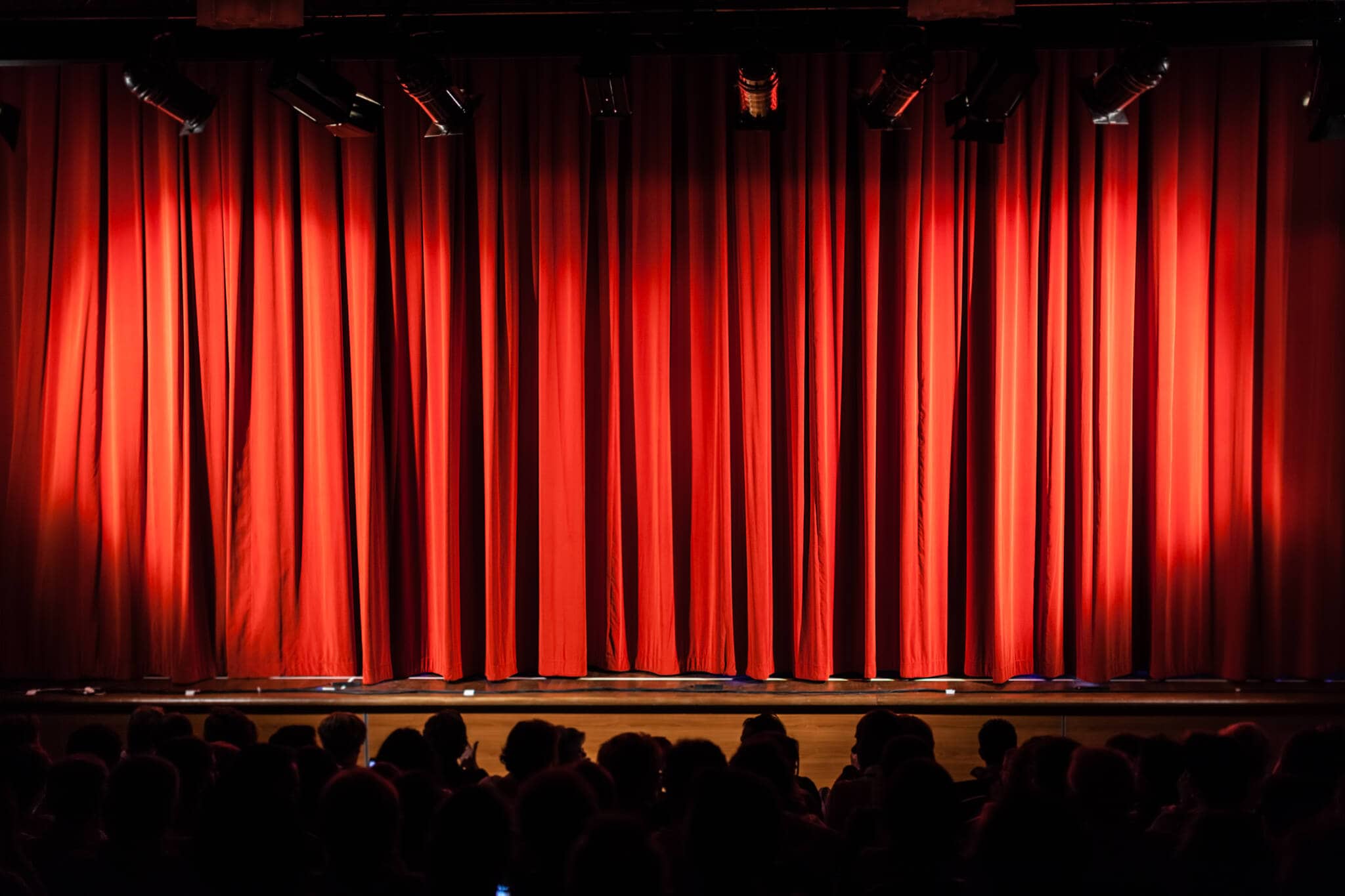 foco de luz apontado para um cortinado vermelho sob um palco que recebe espectáculos culturais