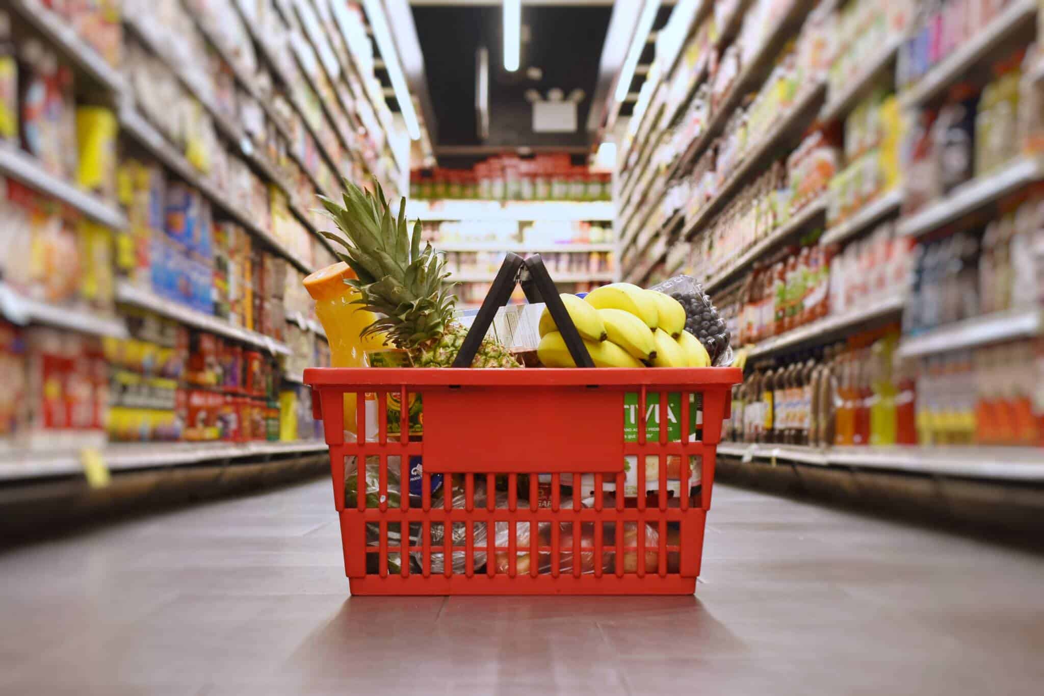cesto de compras no meio do chão de um corredor de supermercado, ilustrando as várias possibilidades de poupar no supermercado