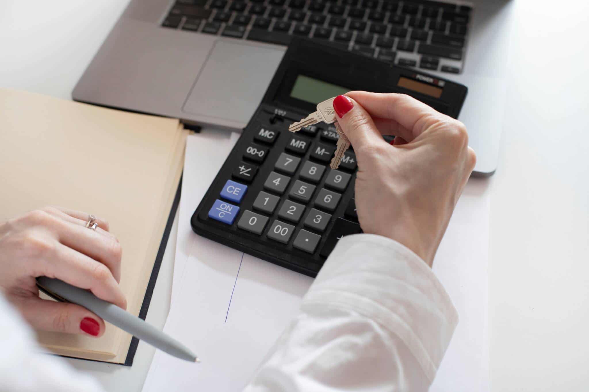 Mãos com calculadora, caderno e portátil a fazer contas para determinar o LTV