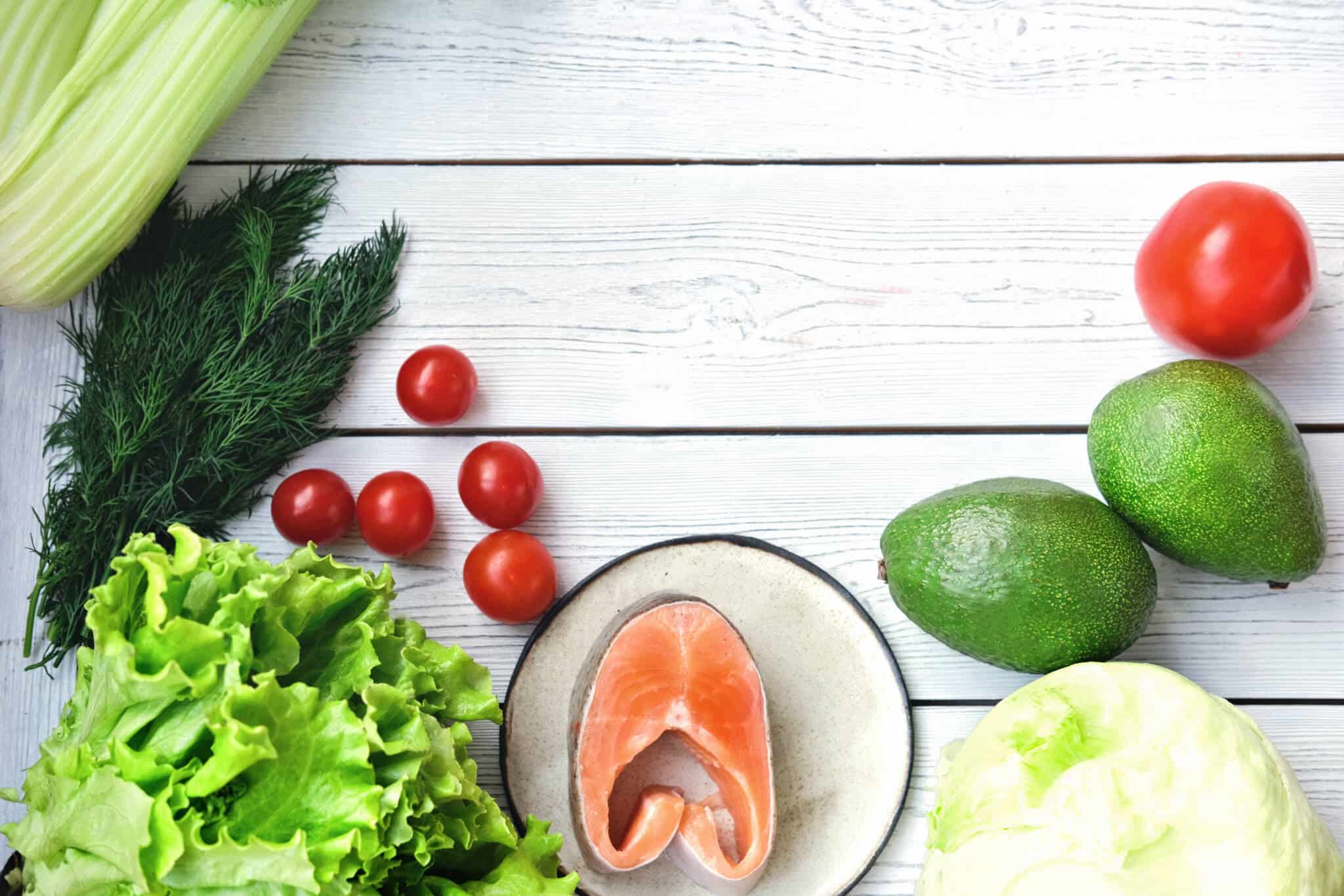 conjunto de alimentos diverso e rico, dispostos em círculo e em fundo branco de uma bancada, remetendo para refeições saudáveis