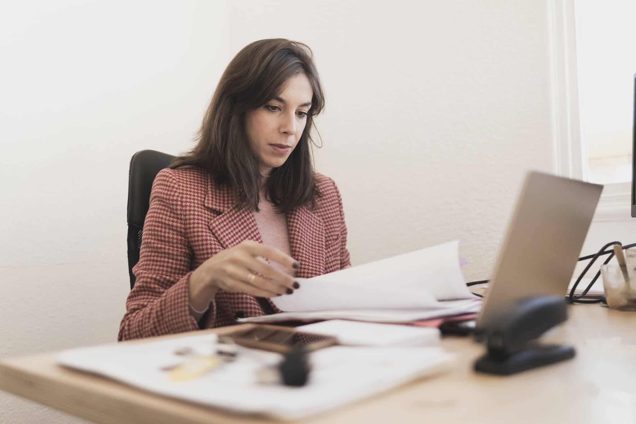 Mulher por detrás de secretária em frente a computador a analisar os documentos necessários para fazer o IRS