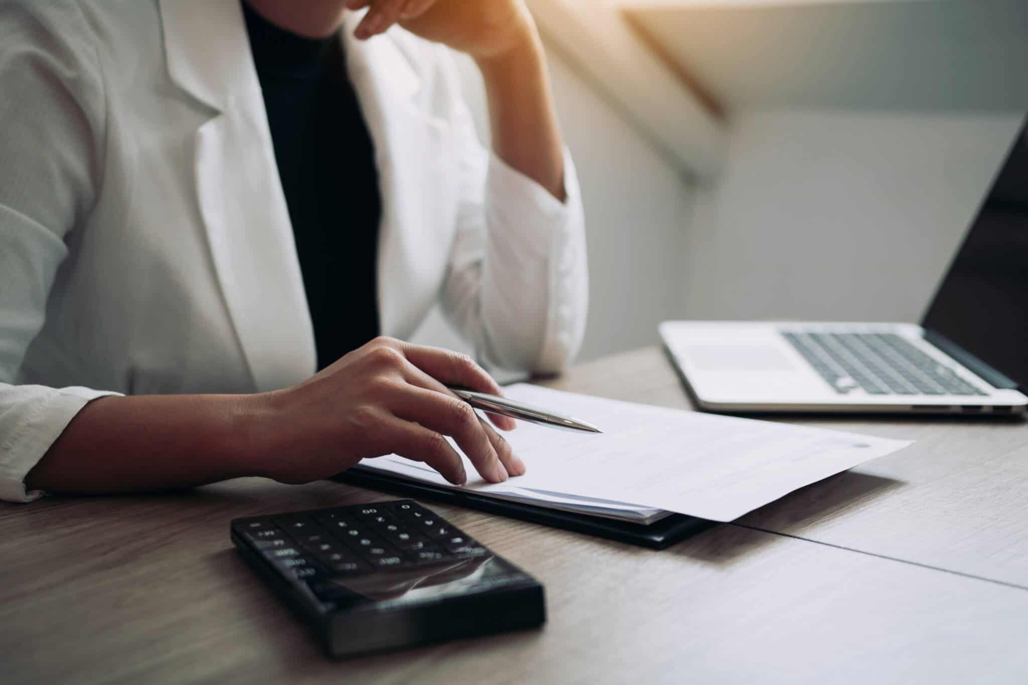 jovem mulher, vestia de blazer branco, formal, usa calculadora e papel para fazer contas e pagar IRS em prestações