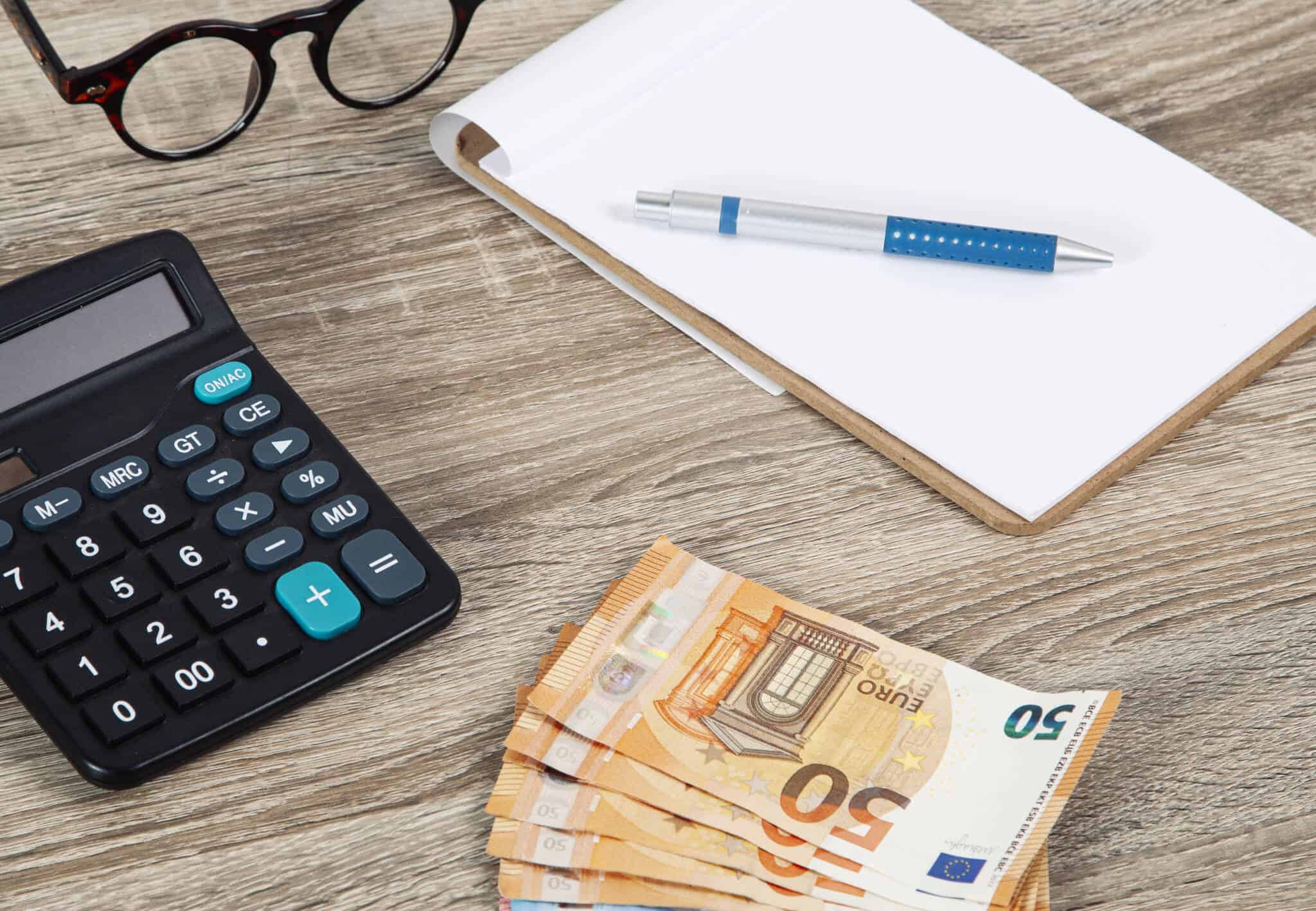mesa com notas de euros, calculadora e um bloco de notas e caneta para ilustrar como utilizar o subsídio de férias para equilibrar as finanças pessoais