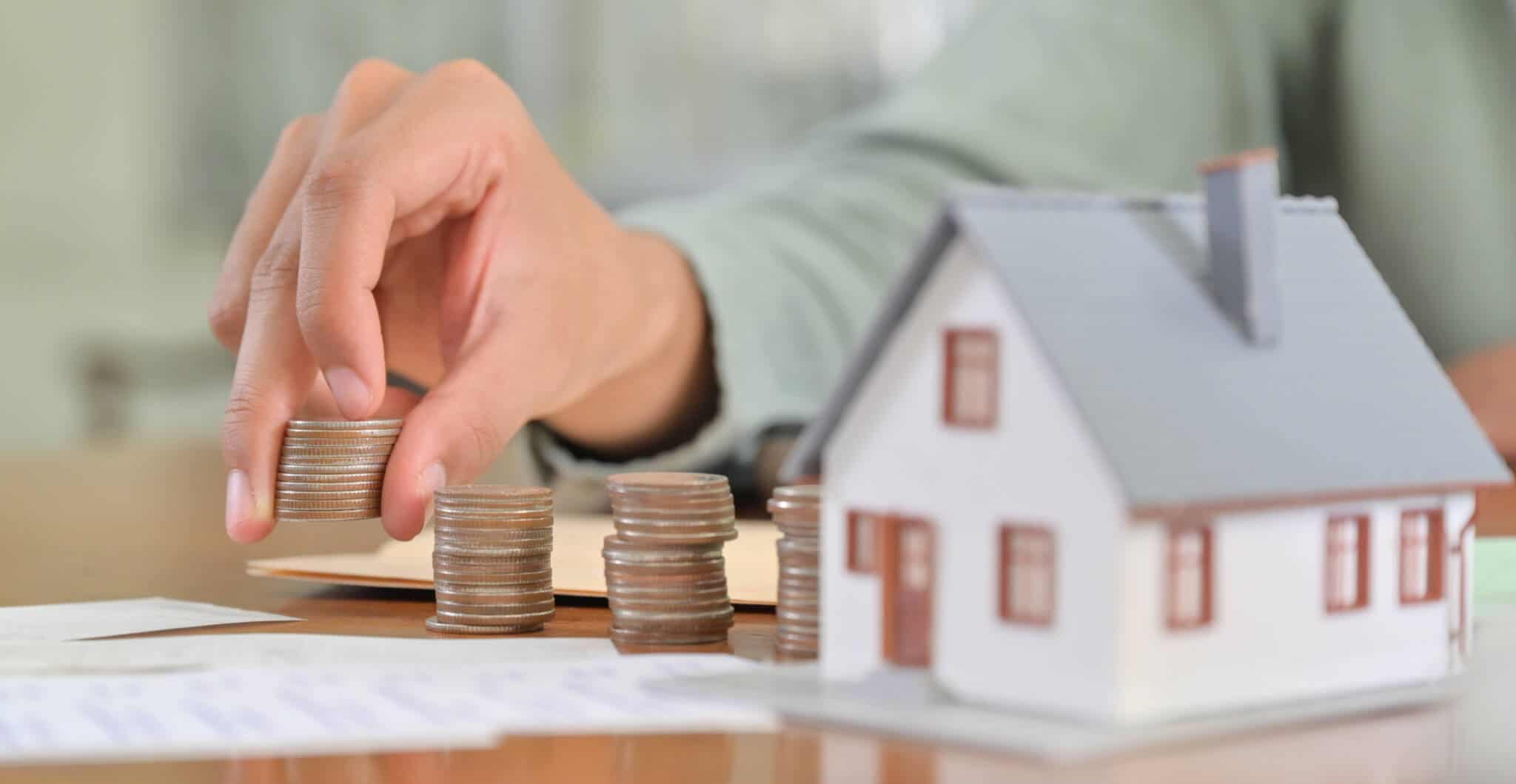 uma casa, com uma pessoa a colocar moedas ao lado e papeis na mesa a ilustrar quanto custa fazer um crédito habitação