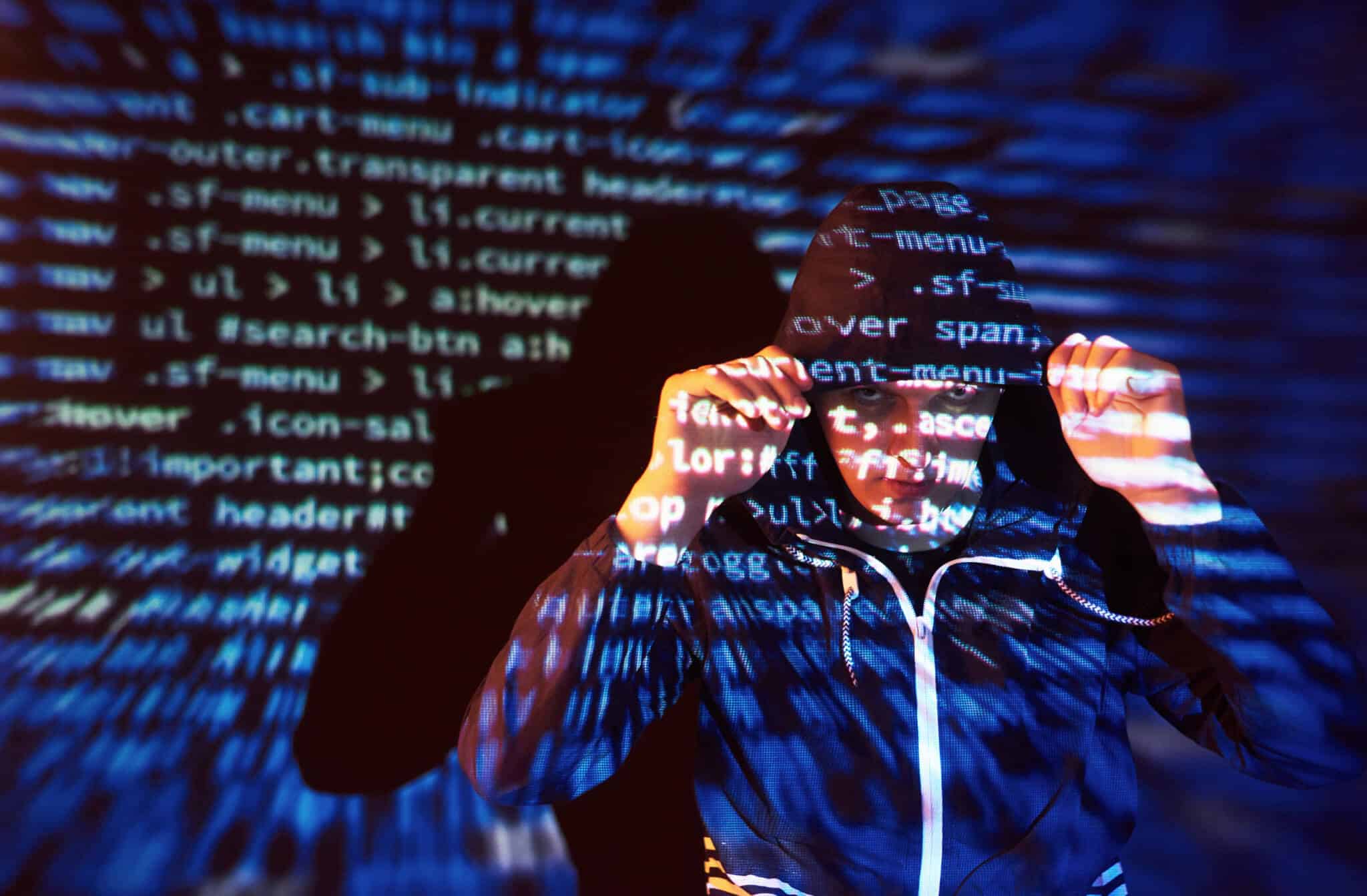 jovem rapaz tapa a cabeça com capuz esta frente a projeções de códigos de programação que permitem o roubo de identidade