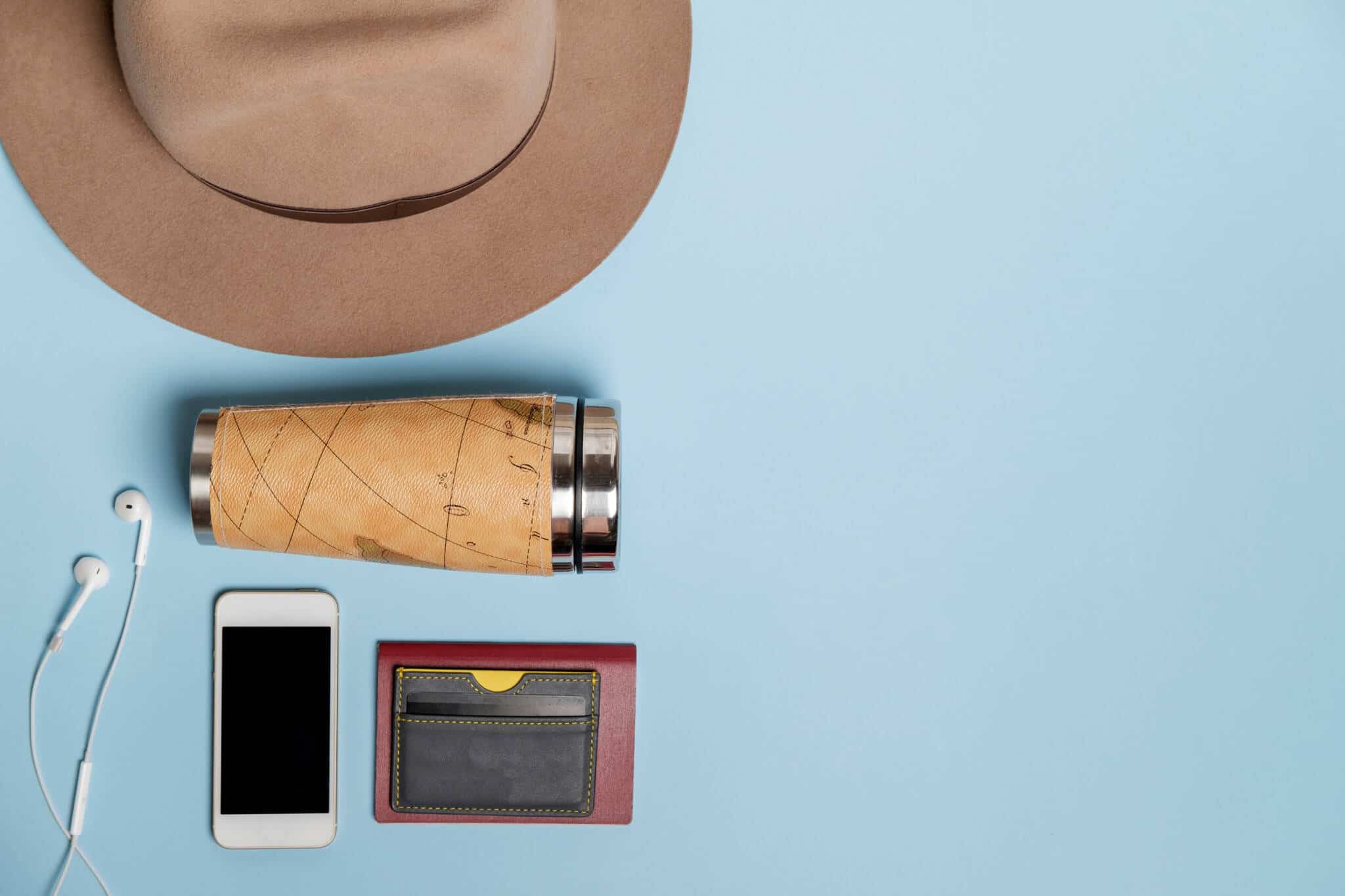 em fundo azul, alguns bojetos, como um chapéu, carteira de cartóes, um telemóvel, uma garrafa de água reutilizável, remetem para os momentos em que vamos viajar e nos quais temos de ter cartões bancários